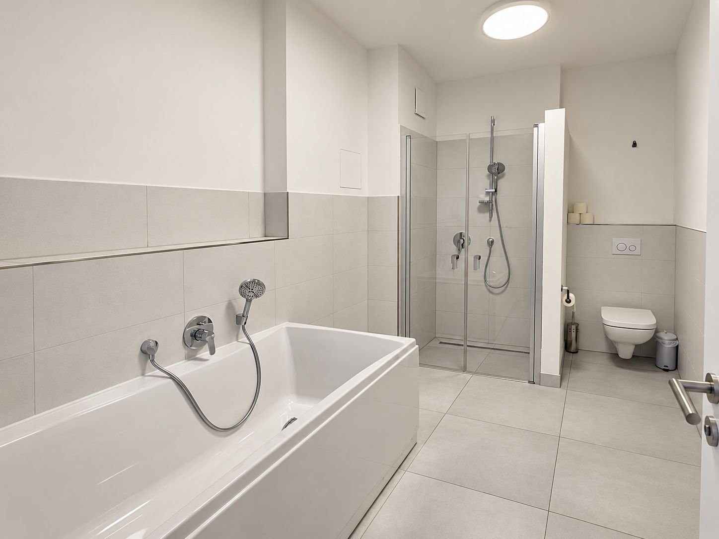 Modernes Badezimmer mit Badewanne, Dusche und WC, hell gefliest.