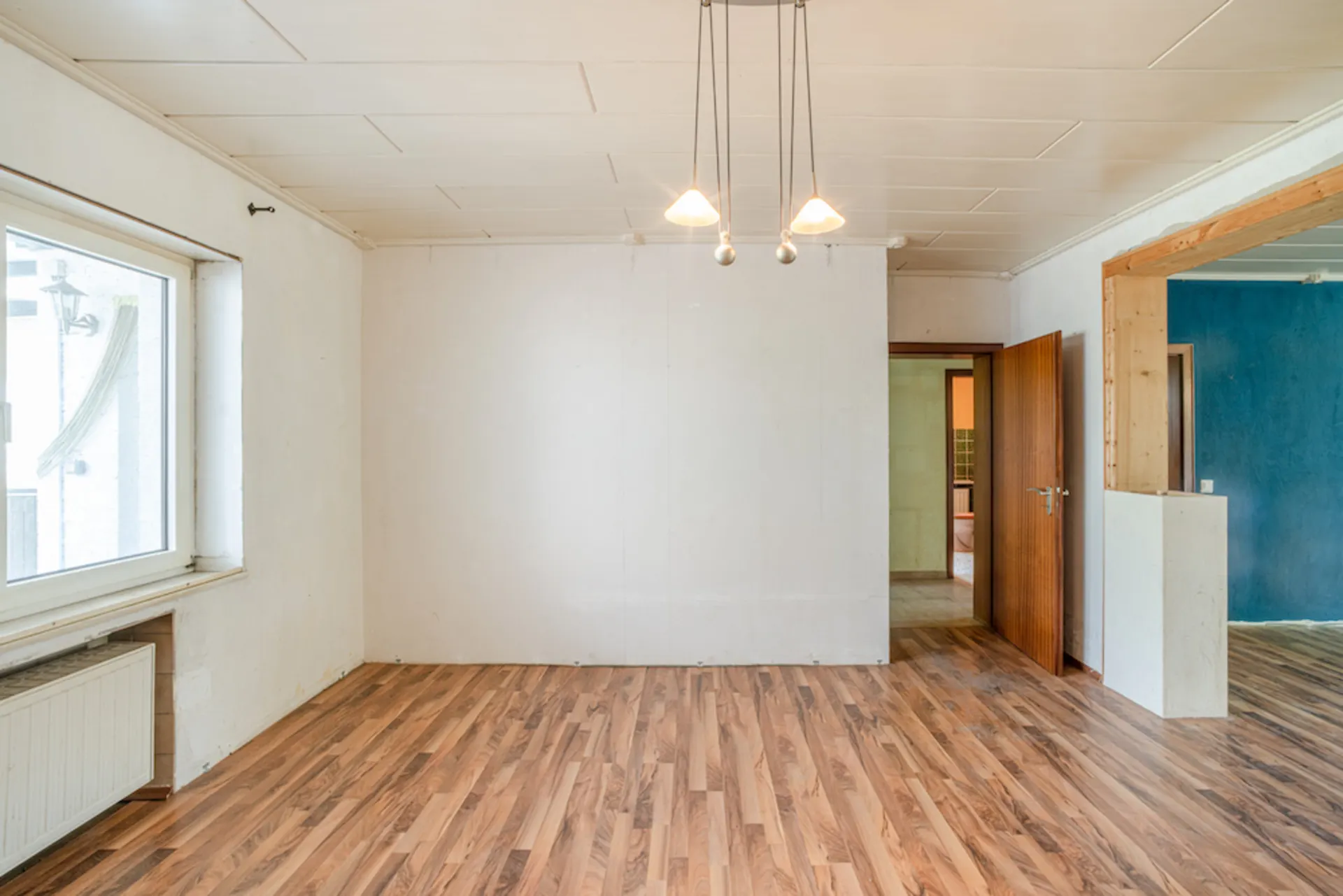 Leerer Raum mit Holzfußboden, Deckenlampe, Fenster und offener Tür.