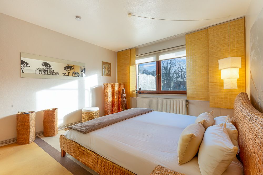 Helles Schlafzimmer mit großem Bett, Korbmöbeln und Fenster mit Blick nach draußen.