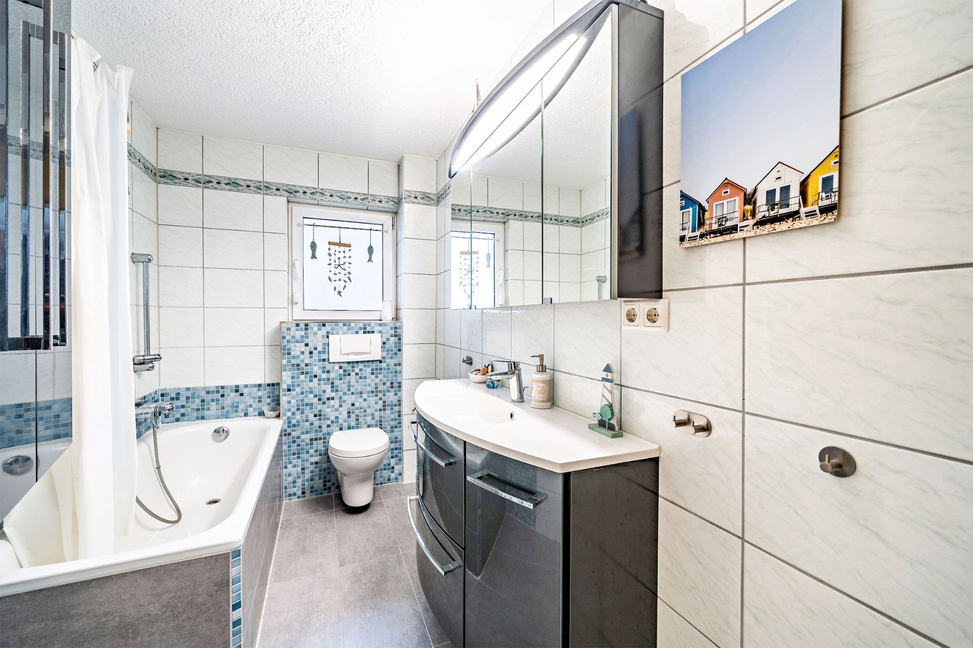 Modernes Badezimmer mit Badewanne, Waschbecken, Spiegel und Toilette, blaue Mosaikfliesen.