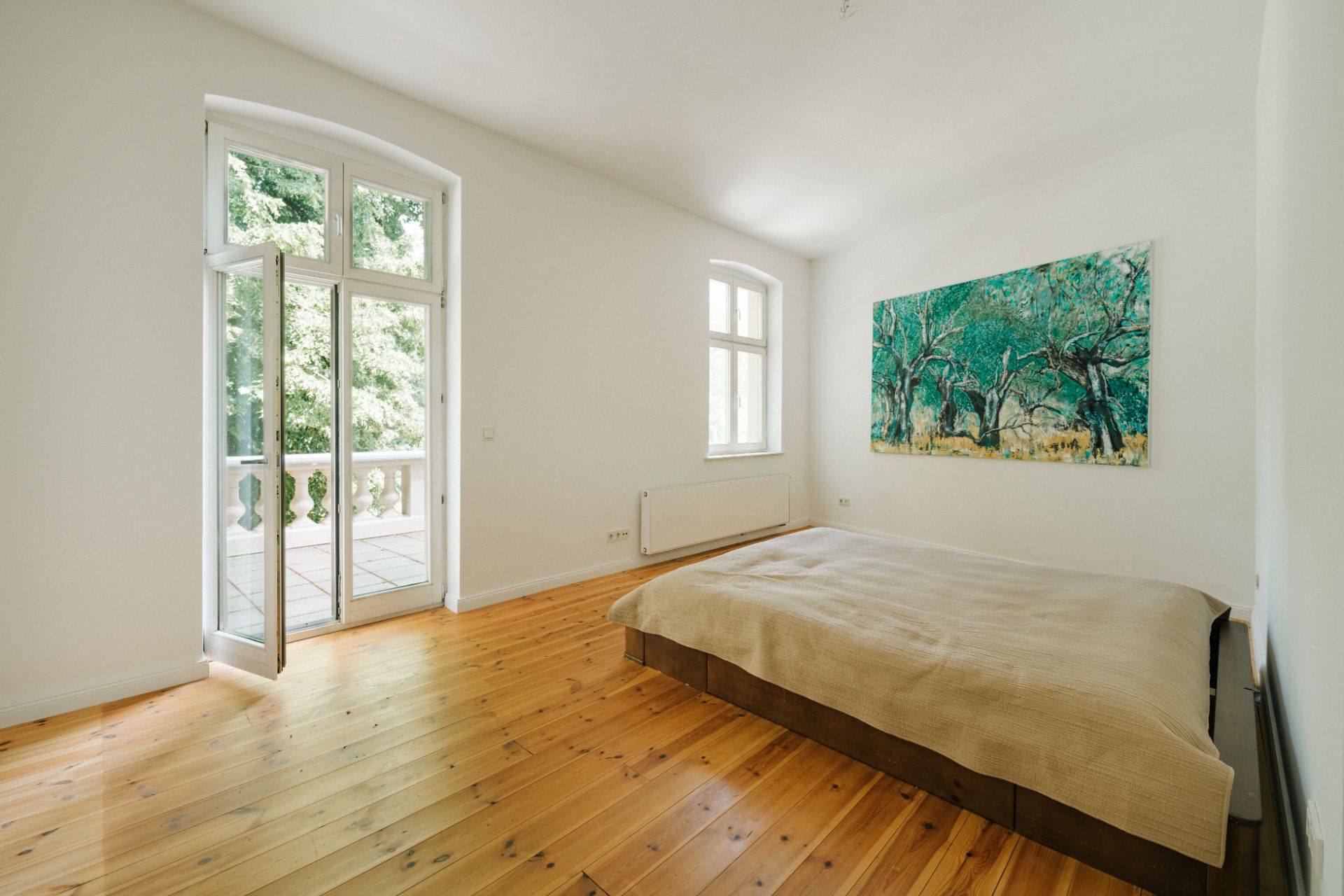 Helles Schlafzimmer mit Holzboden, großem Fenster, Balkonzugang und einem Bett.