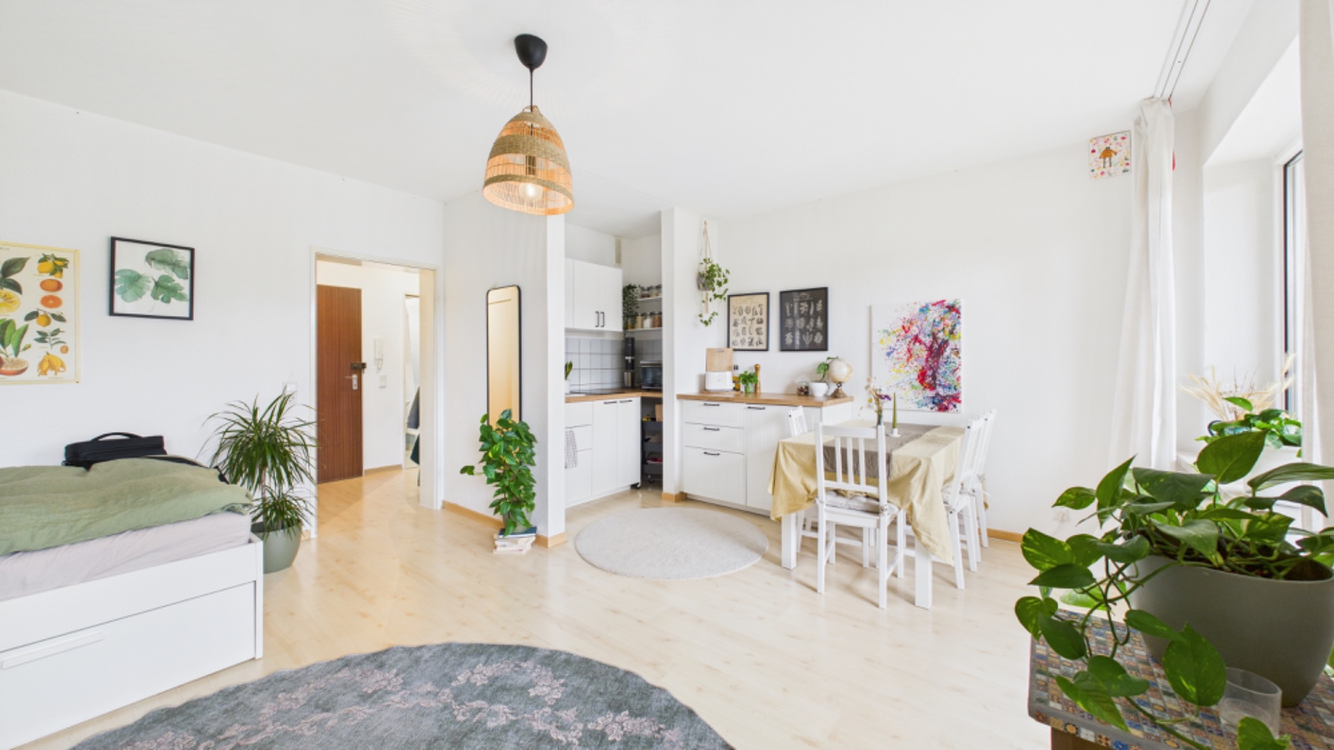 Helles Einzimmer-Apartment mit Küche, Esstisch, Bett und mehreren Zimmerpflanzen.