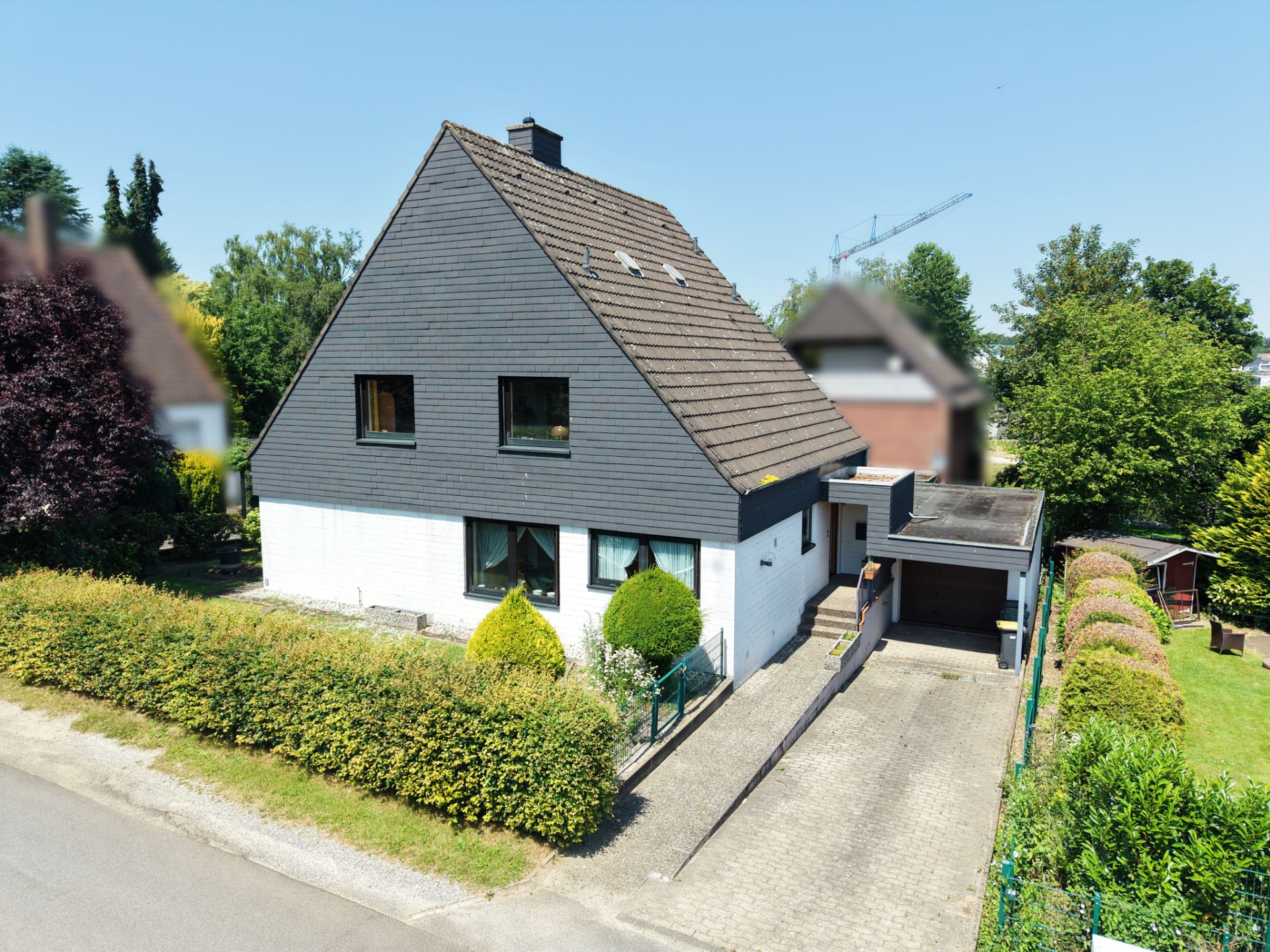 Zweistöckiges Einfamilienhaus mit dunklem Satteldach, Vorgarten und Auffahrt mit Carport.