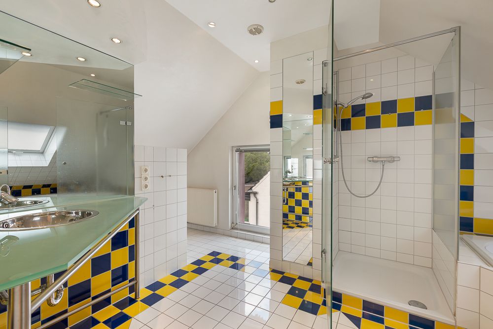 Modernes Badezimmer mit Glaswaschtisch, Dusche und bunten Fliesen in Blau und Gelb.