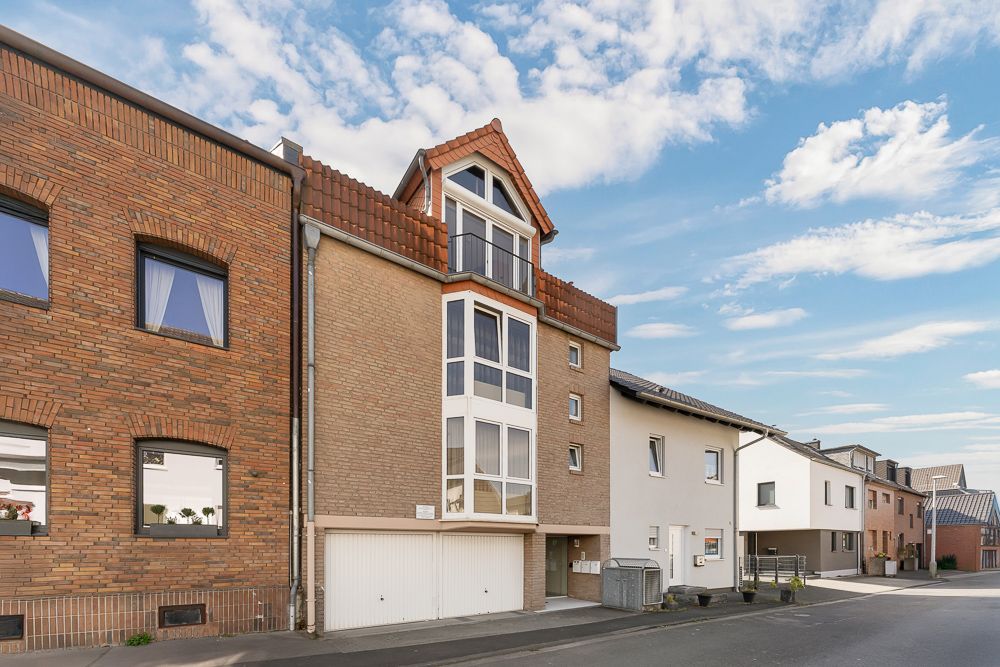 Mehrstöckiges Wohnhaus mit großem Erkerfenster und Garagentor an einer ruhigen Straße.