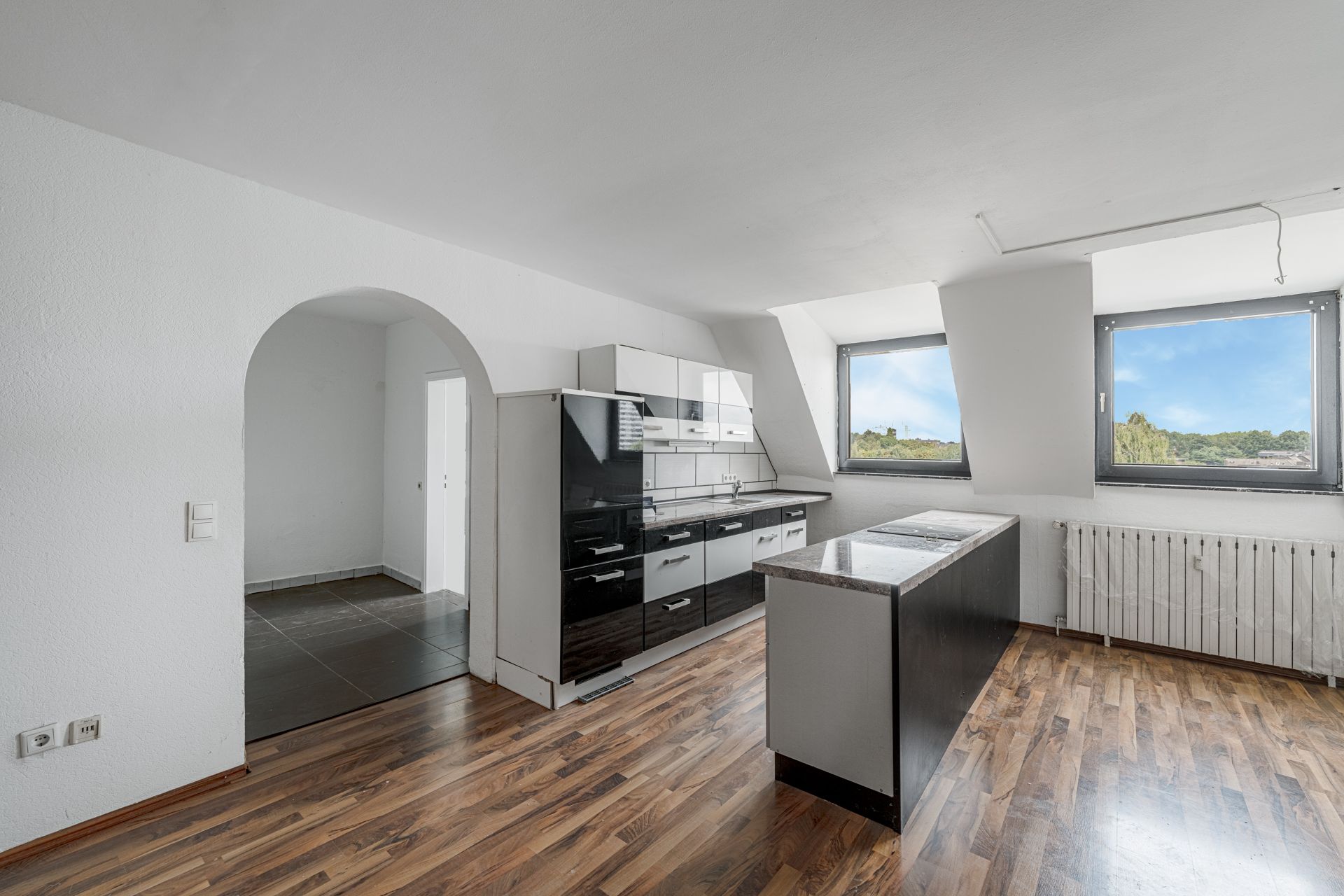 Helle Küche mit Küchenzeile, Kochinsel, Holzboden und zwei Fenstern mit Ausblick.