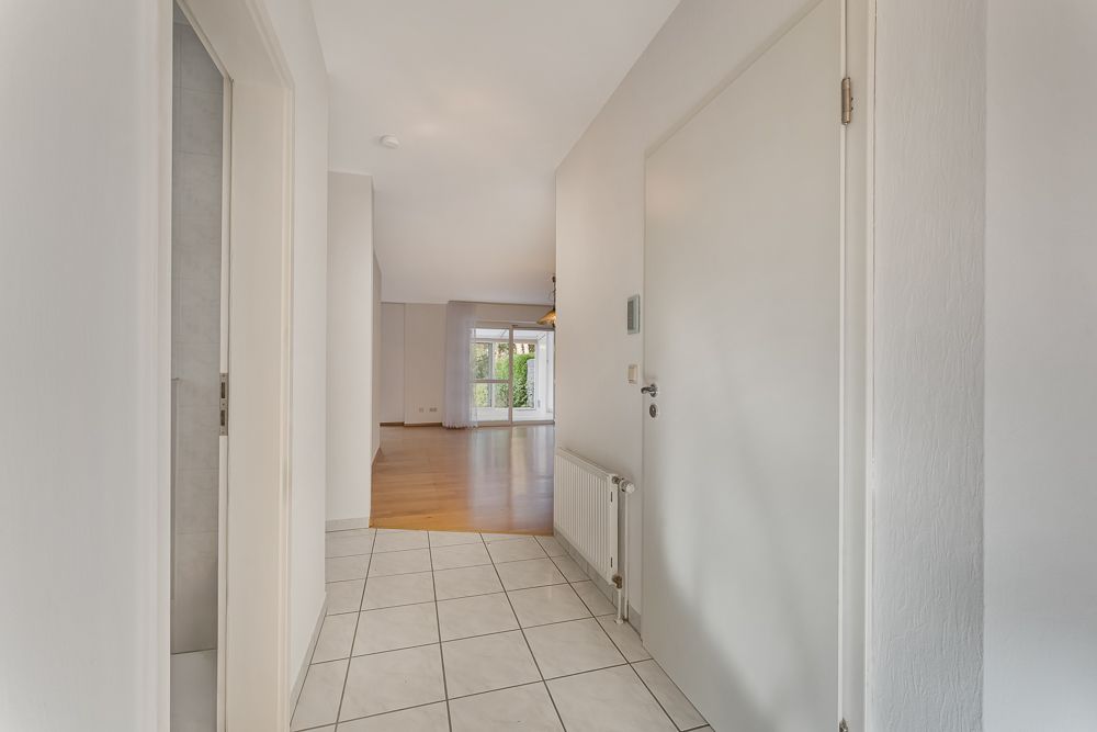 Heller Flur mit Fliesenboden, Türen und Blick auf ein Wohnzimmer mit Parkettboden.