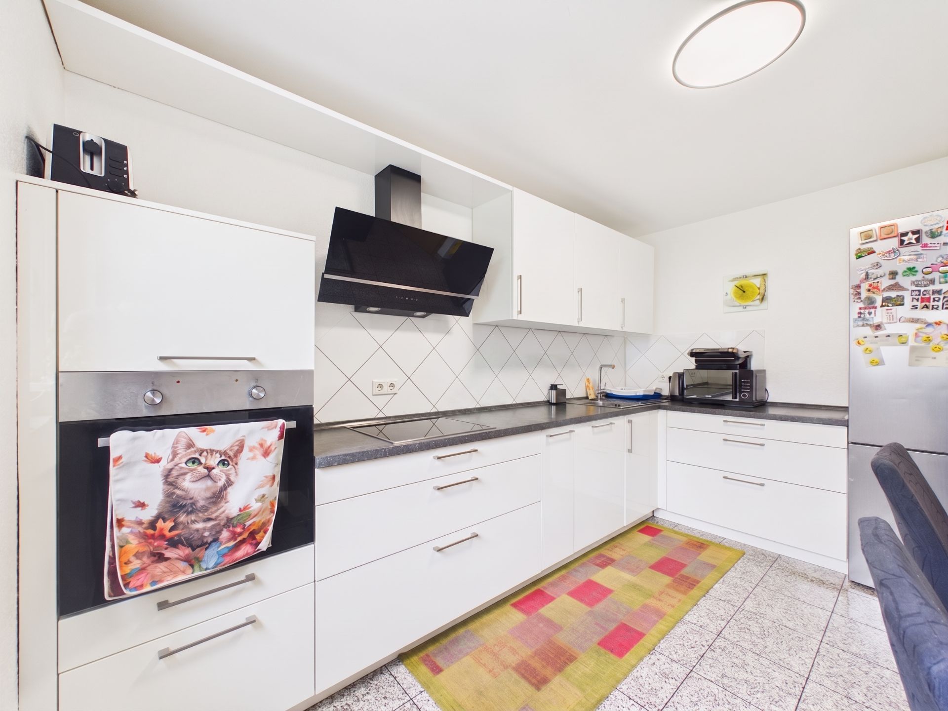 Moderne Küche mit weißen Schränken, buntem Teppich und Kühlschrank mit Magneten.