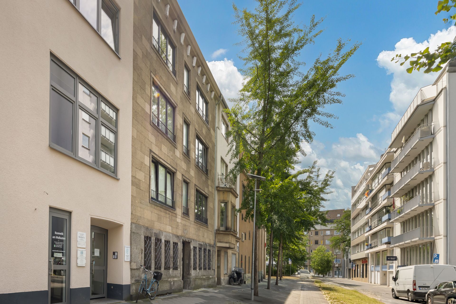 Mehrstöckige Wohngebäude an einer ruhigen, baumbestandenen Straße mit Gehweg.