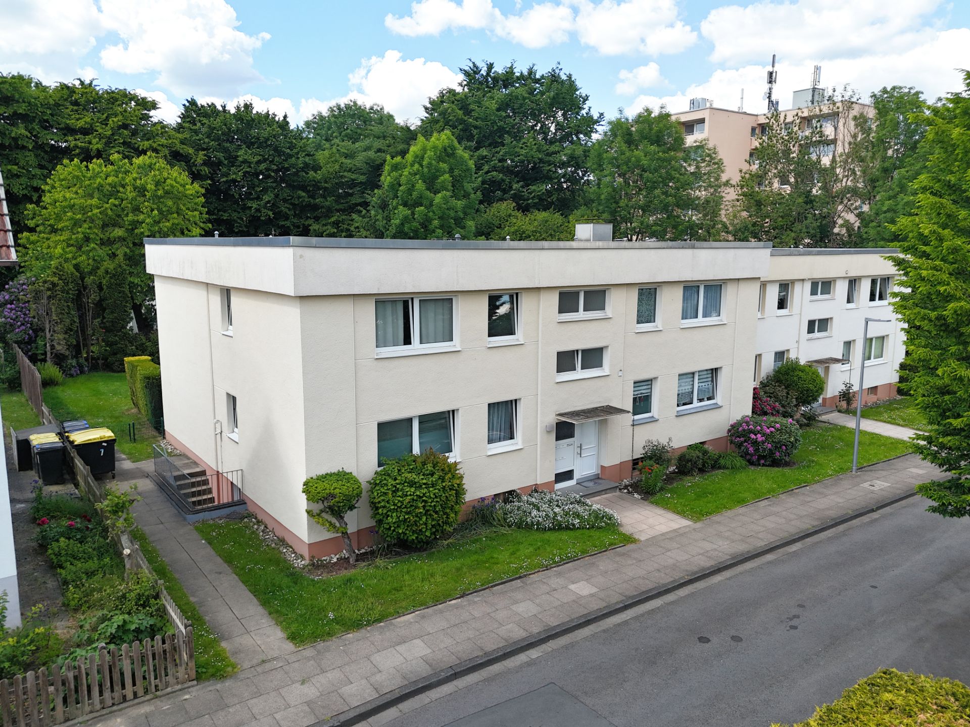 Zweistöckiges Wohnhaus mit flachem Dach, Vorgarten und Gehweg, umgeben von Bäumen.