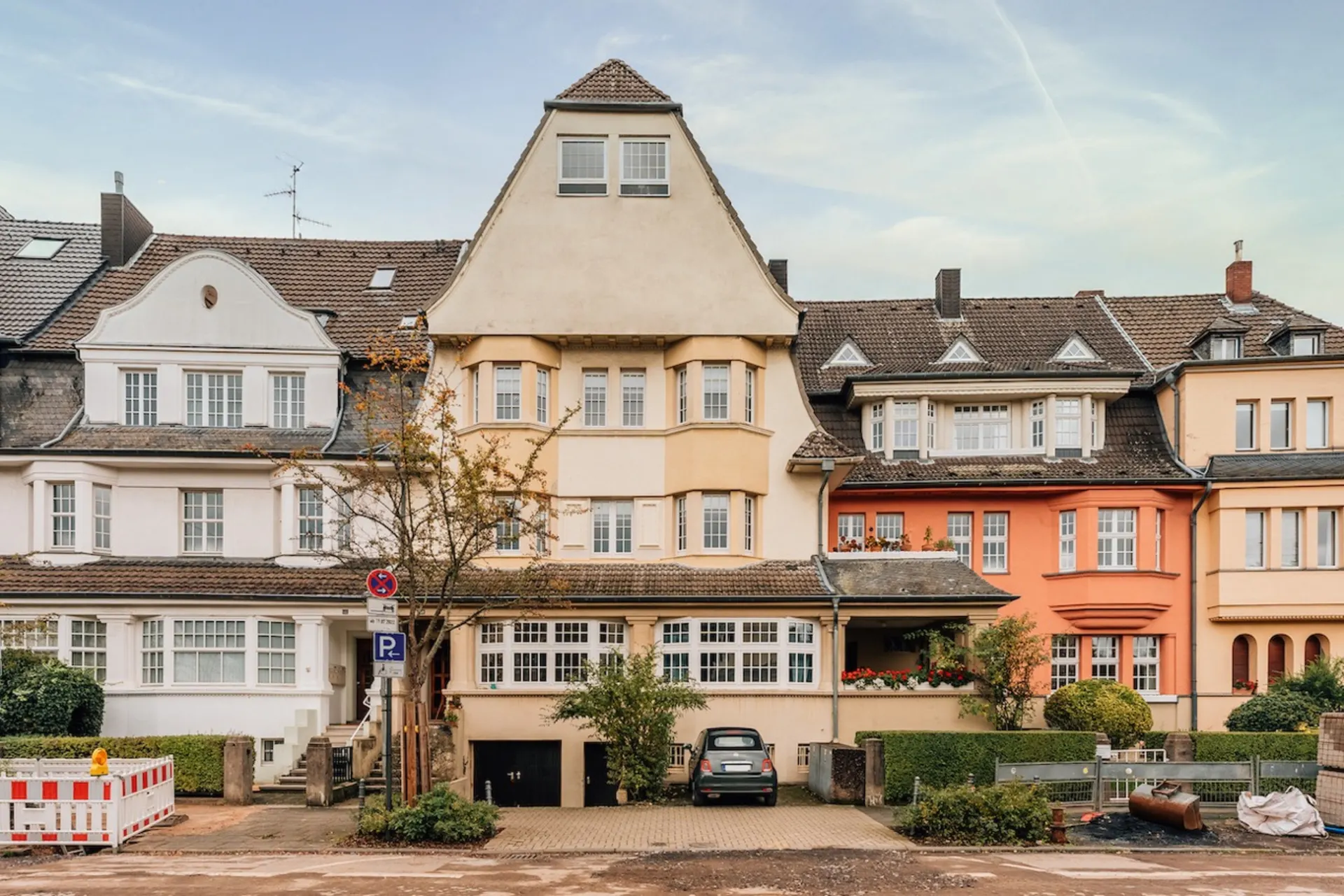 Mehrstöckiges Wohnhaus mit Erker, Auffahrt und geparktem Auto, daneben weitere Wohnhäuser.