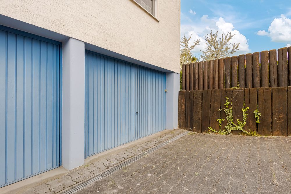 Zwei blaue Garagentore an einem Wohngebäude neben einem Holzzaun.