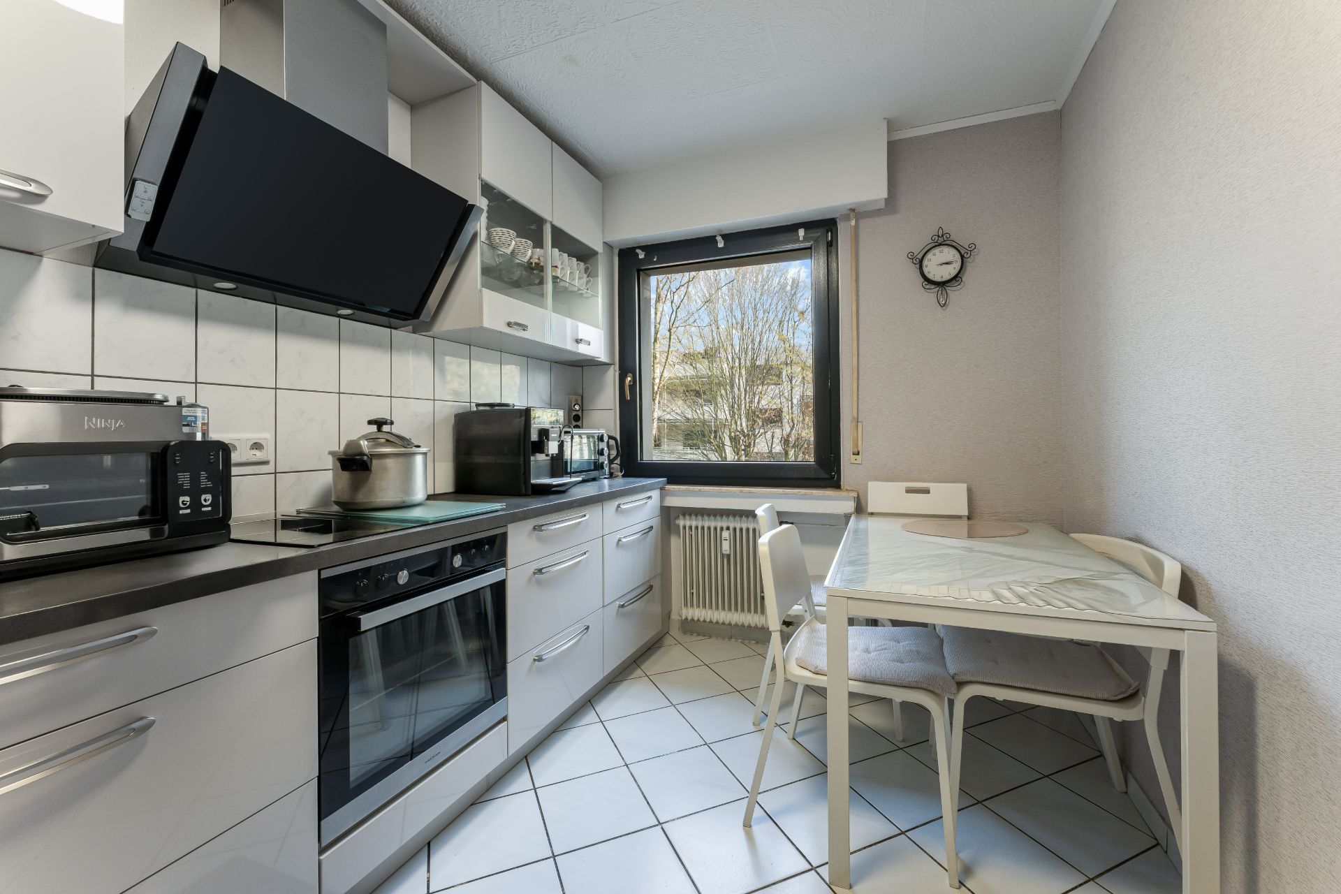 Helle Küche mit Esstisch, Stühlen, Herd, Backofen und großem Fenster mit Blick nach draußen.