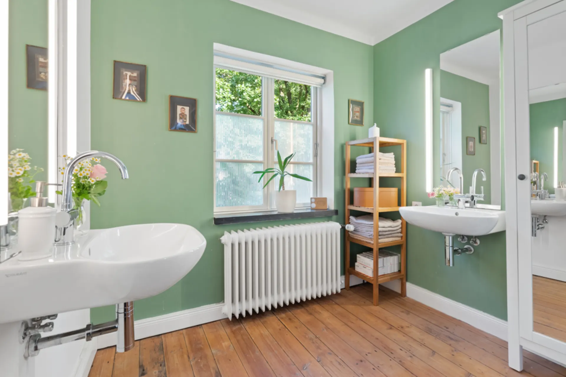 Helles Badezimmer mit grüner Wand, Holzregal, zwei Waschbecken und großem Fenster.
