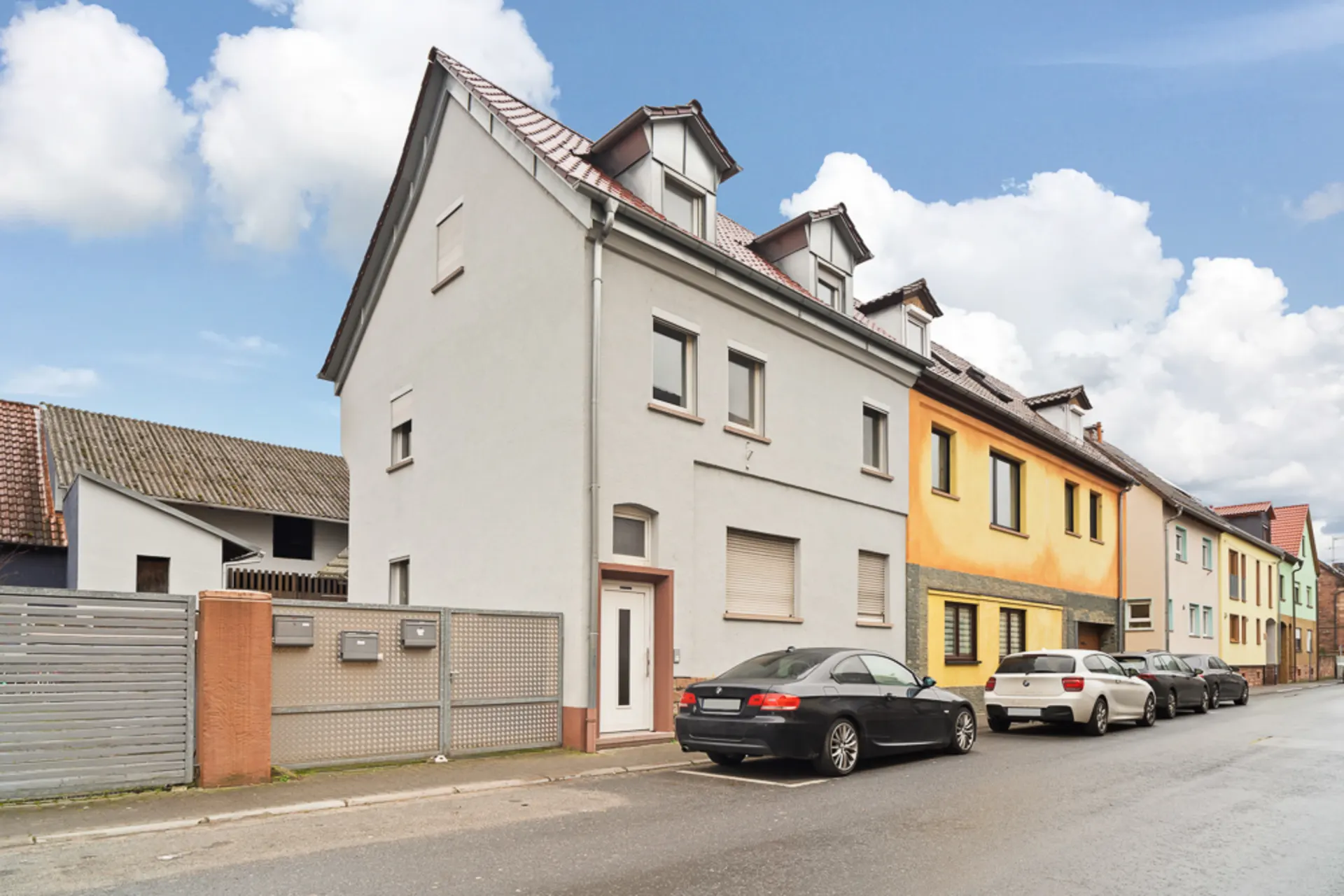 Mehrstöckiges Wohnhaus mit weißer Fassade an einer ruhigen Straße, Autos parken davor.