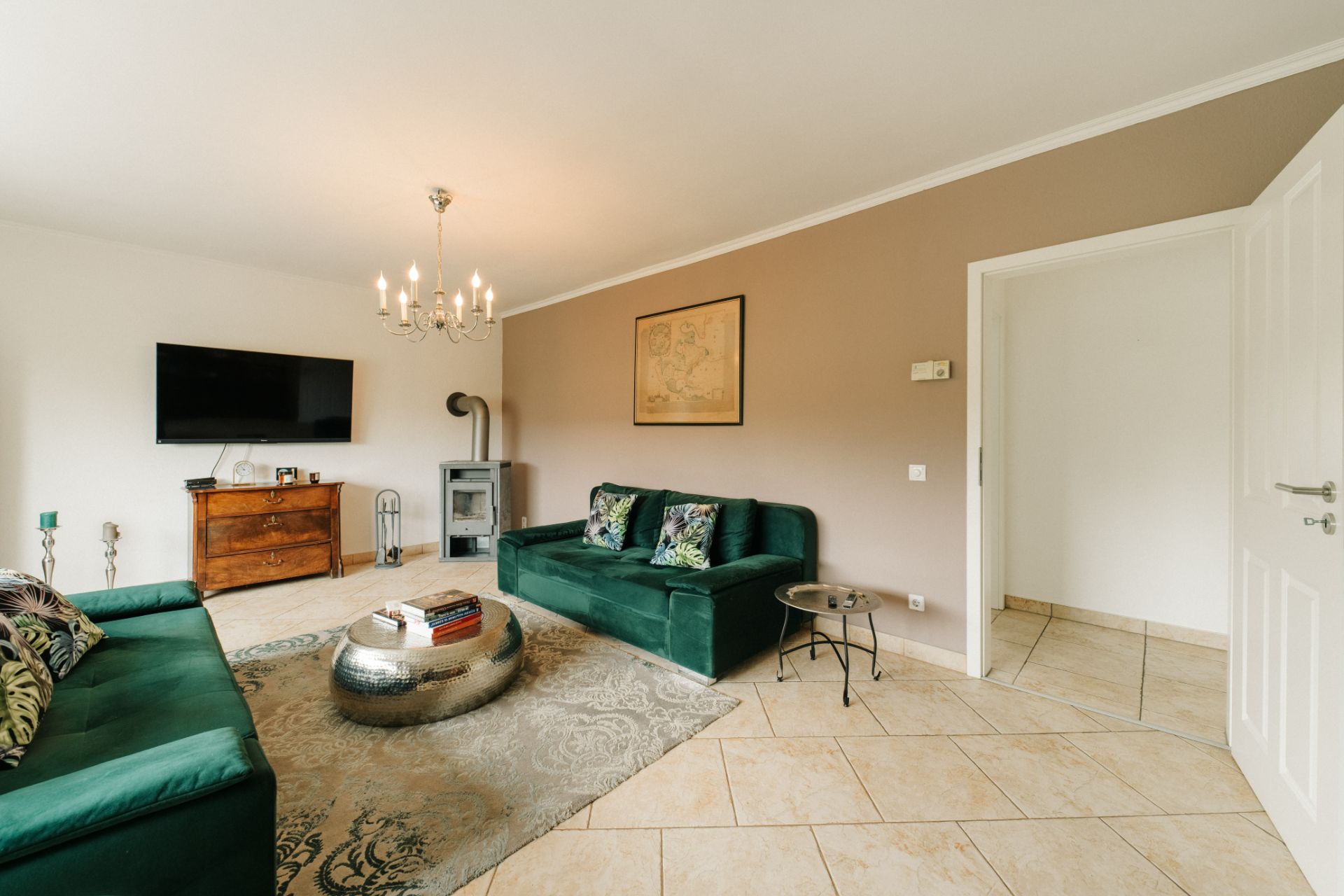 Wohnzimmer mit zwei grünen Sofas, Fernseher, Holzofen und Teppich auf Fliesenboden.