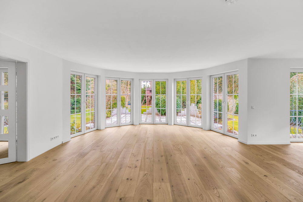 Heller, leerer Raum mit großen bodentiefen Fenstern und Holzfußboden, Blick in den Garten.