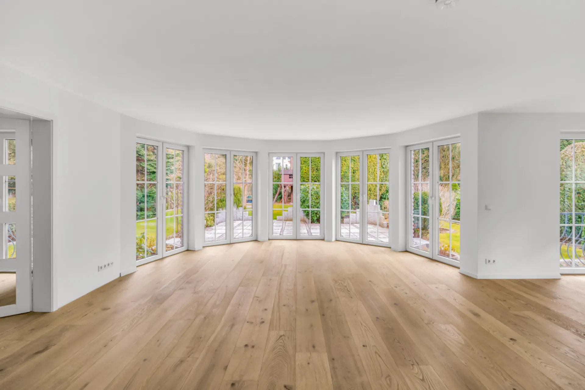 Heller, leerer Raum mit großen bodentiefen Fenstern und Holzfußboden, Blick in den Garten.