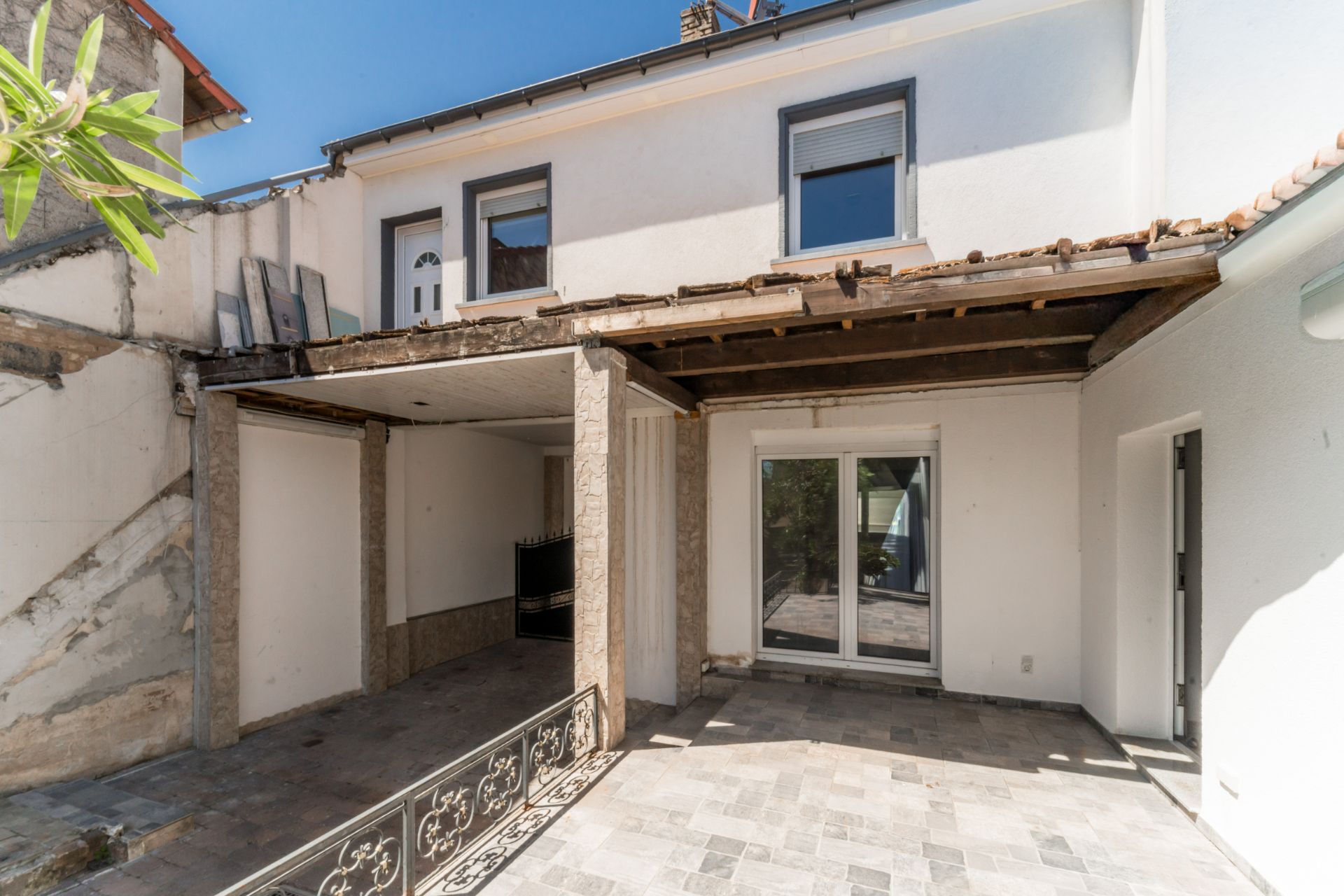Innenhof mit überdachter Terrasse, gefliestem Boden und Zugang zu einem weißen Wohnhaus.
