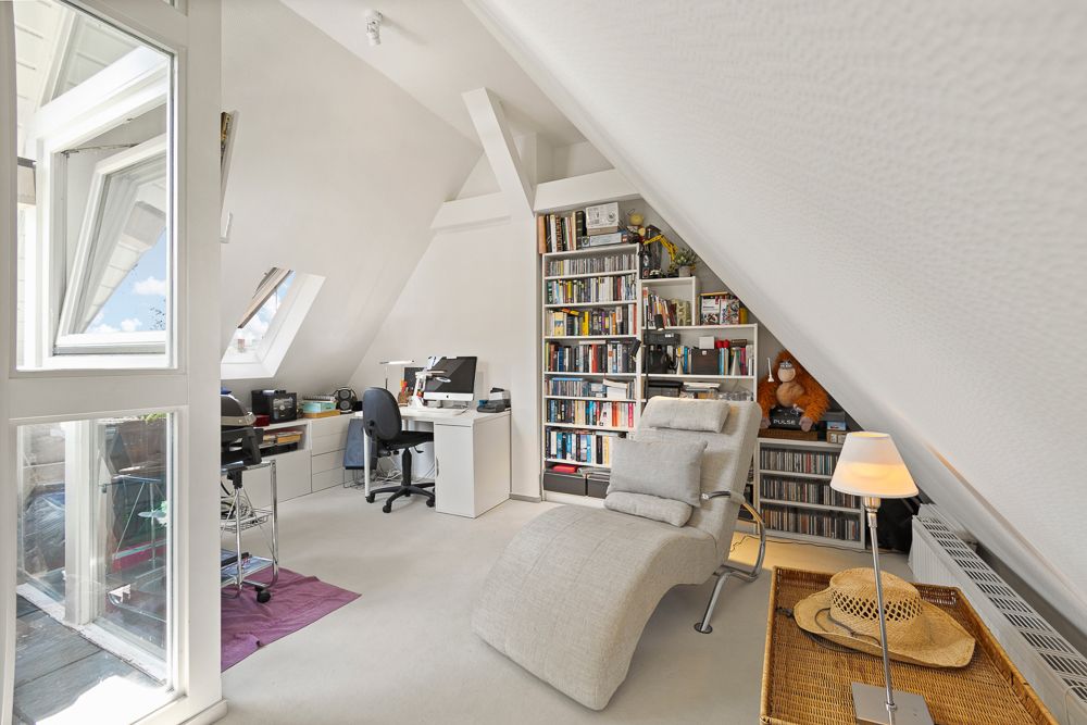Helles Arbeitszimmer mit Schreibtisch, Bücherregal und Liegestuhl unter einem Dachschrägenfenster.