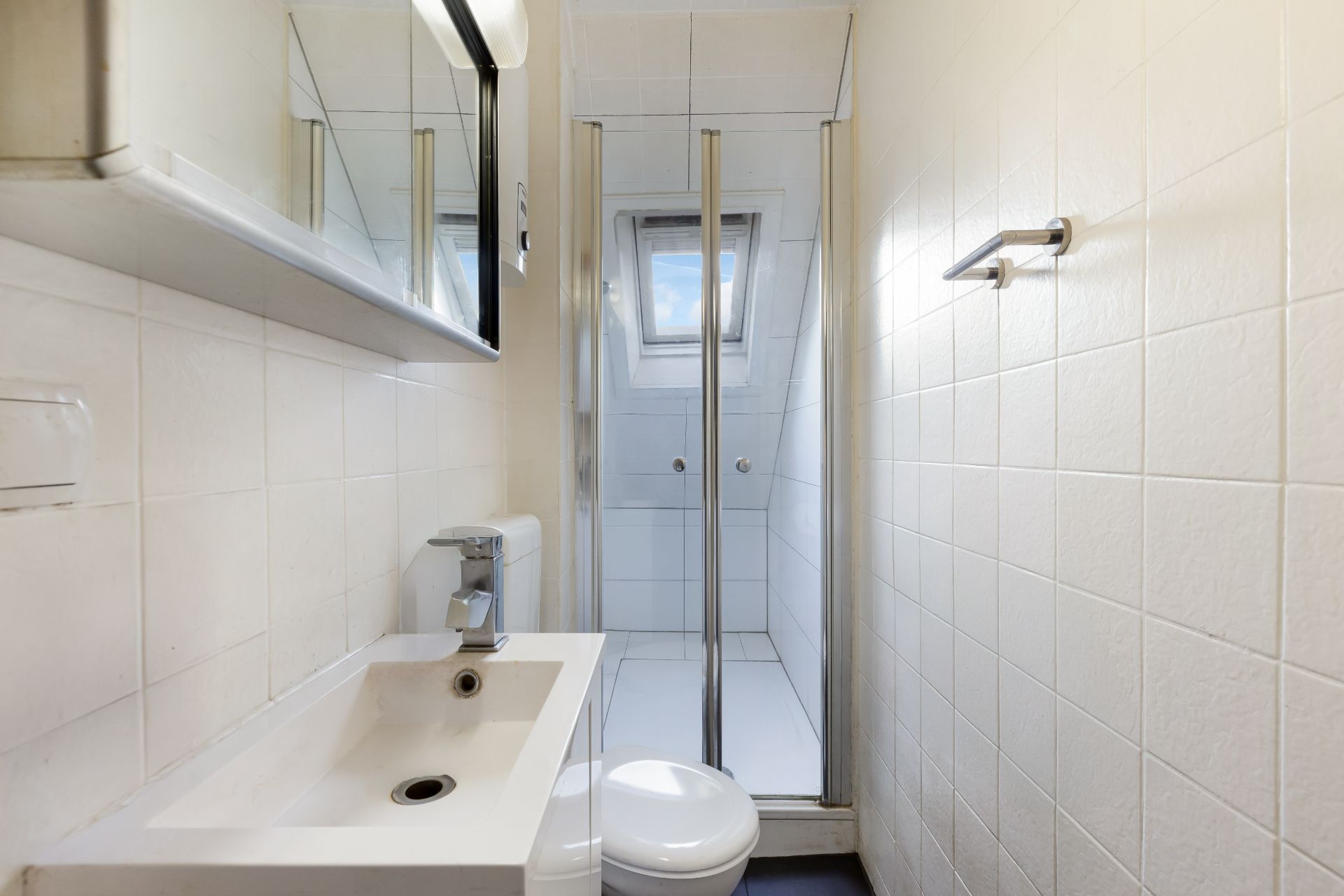 Kleines Badezimmer mit Waschbecken, Toilette und Dusche mit Glaswand sowie einem Fenster.