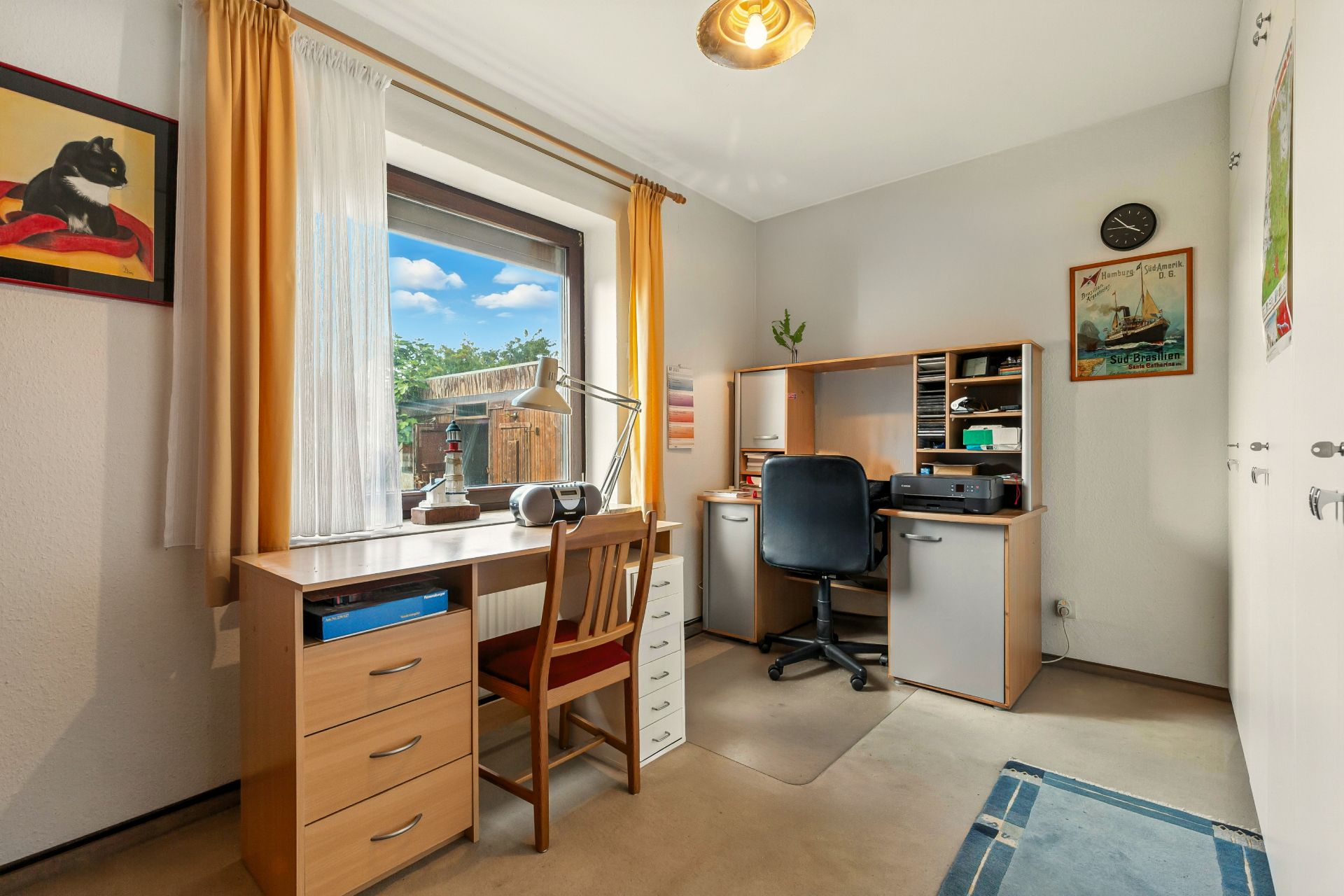 Helles Arbeitszimmer mit zwei Schreibtischen, Regalen, Stuhl und Fenster mit Blick nach draußen.