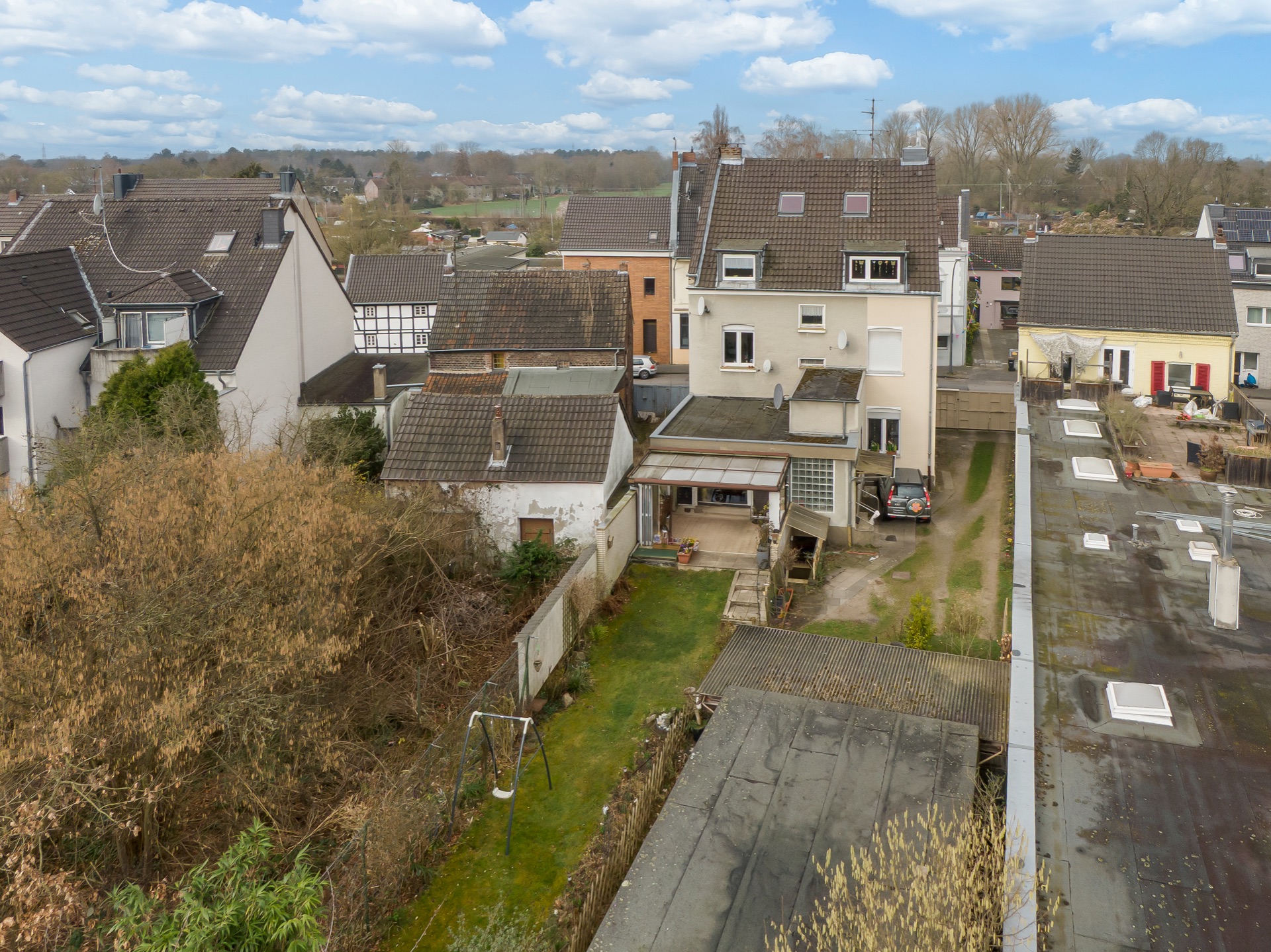 Blick von oben auf ein Wohnhaus mit Garten, Nebengebäuden und umliegenden Häusern.