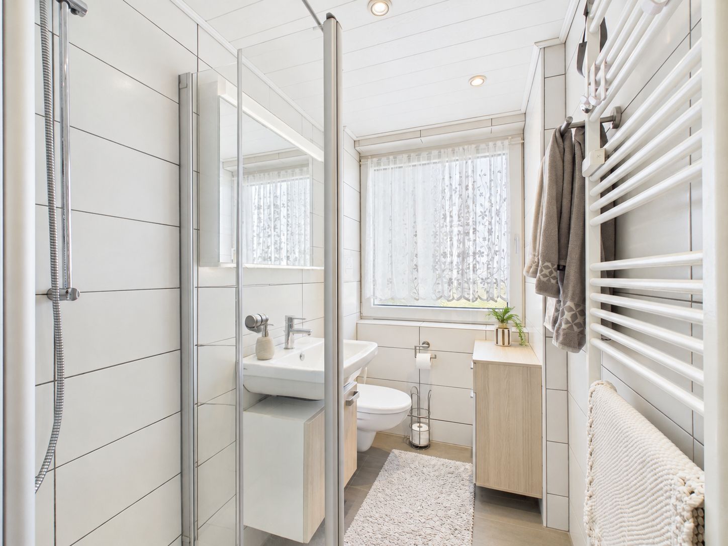 Helles, modernes Badezimmer mit Dusche, Waschbecken, Toilette und Handtuchheizkörper.