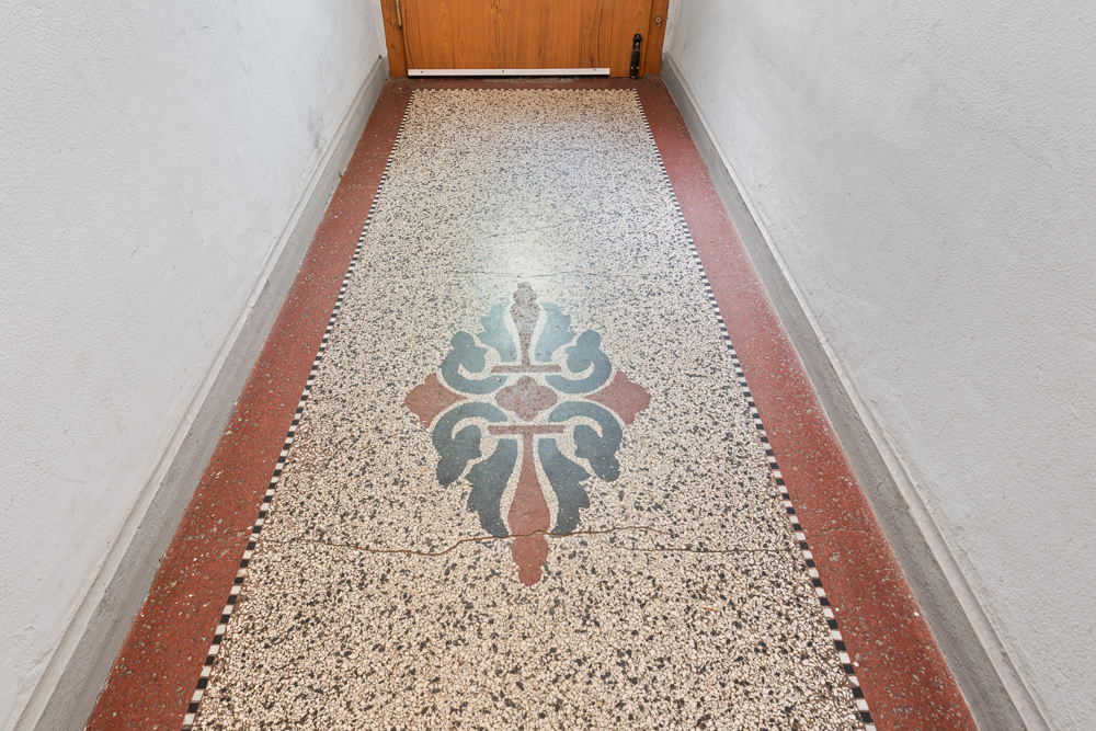 Flur mit Terrazzo-Boden und farbigem Ornament in der Mitte.