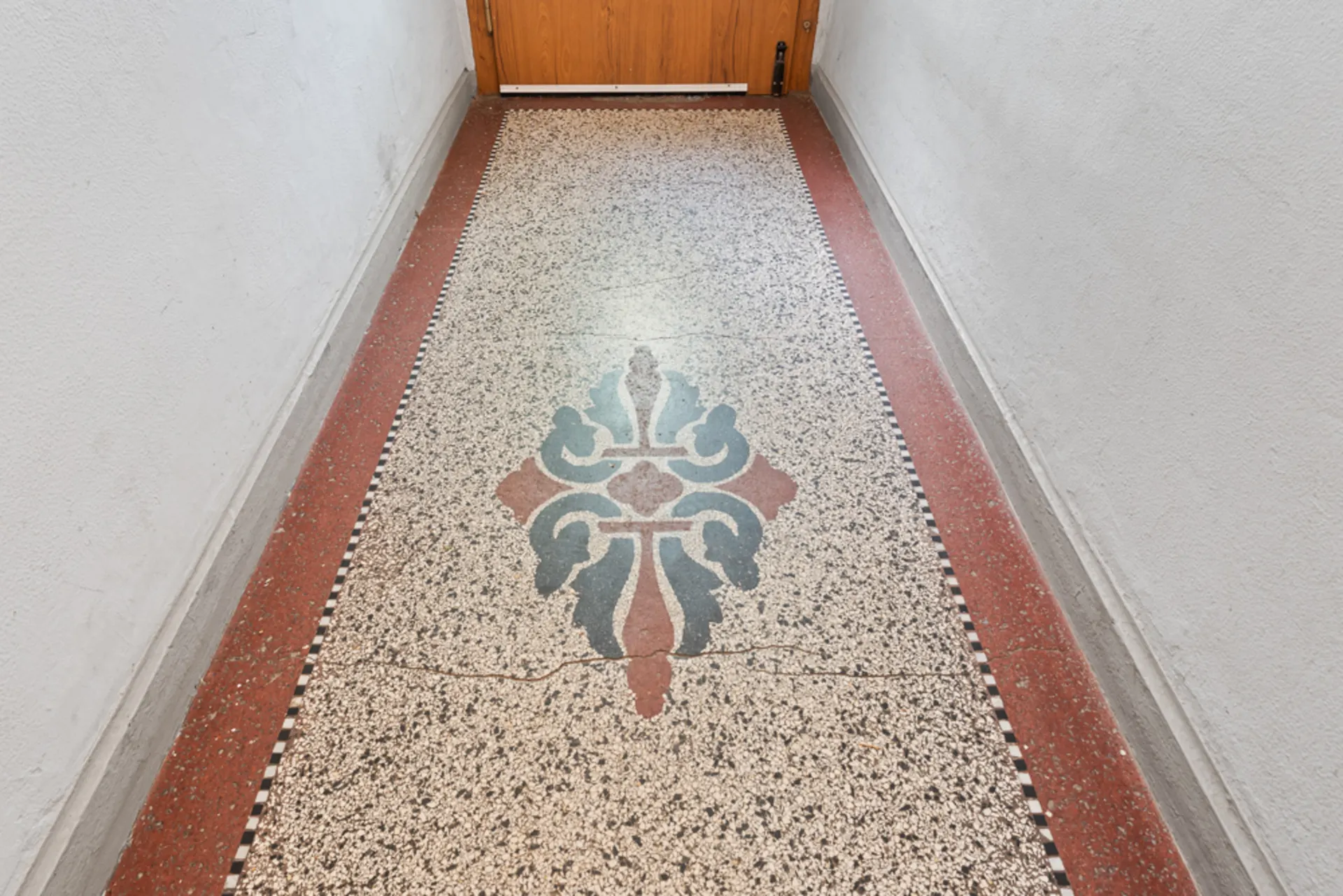 Flur mit Terrazzo-Boden und farbigem Ornament in der Mitte.