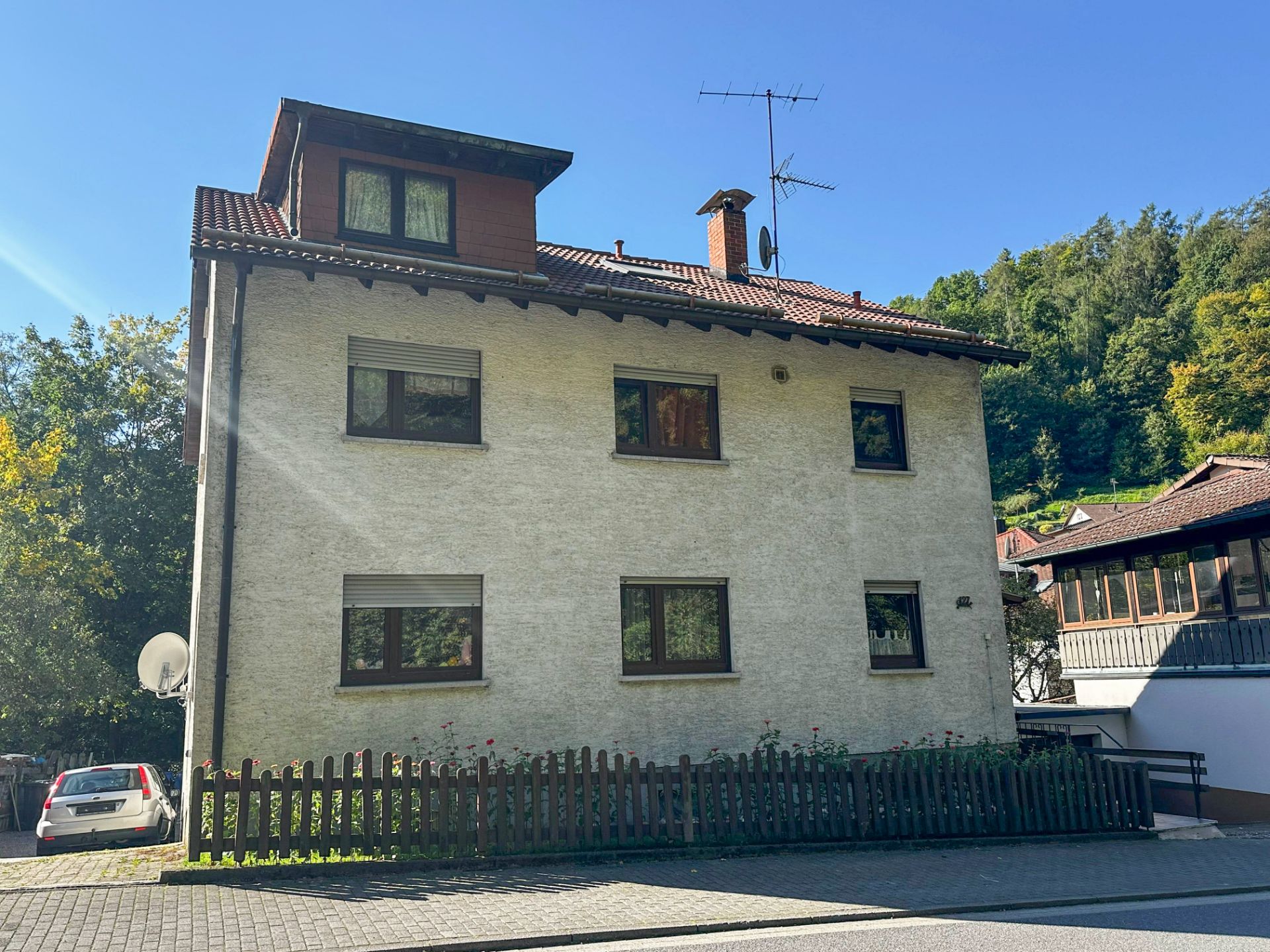 Zweistöckiges Wohnhaus mit Satteldach, Holzzaun und mehreren Fenstern an der Fassade.