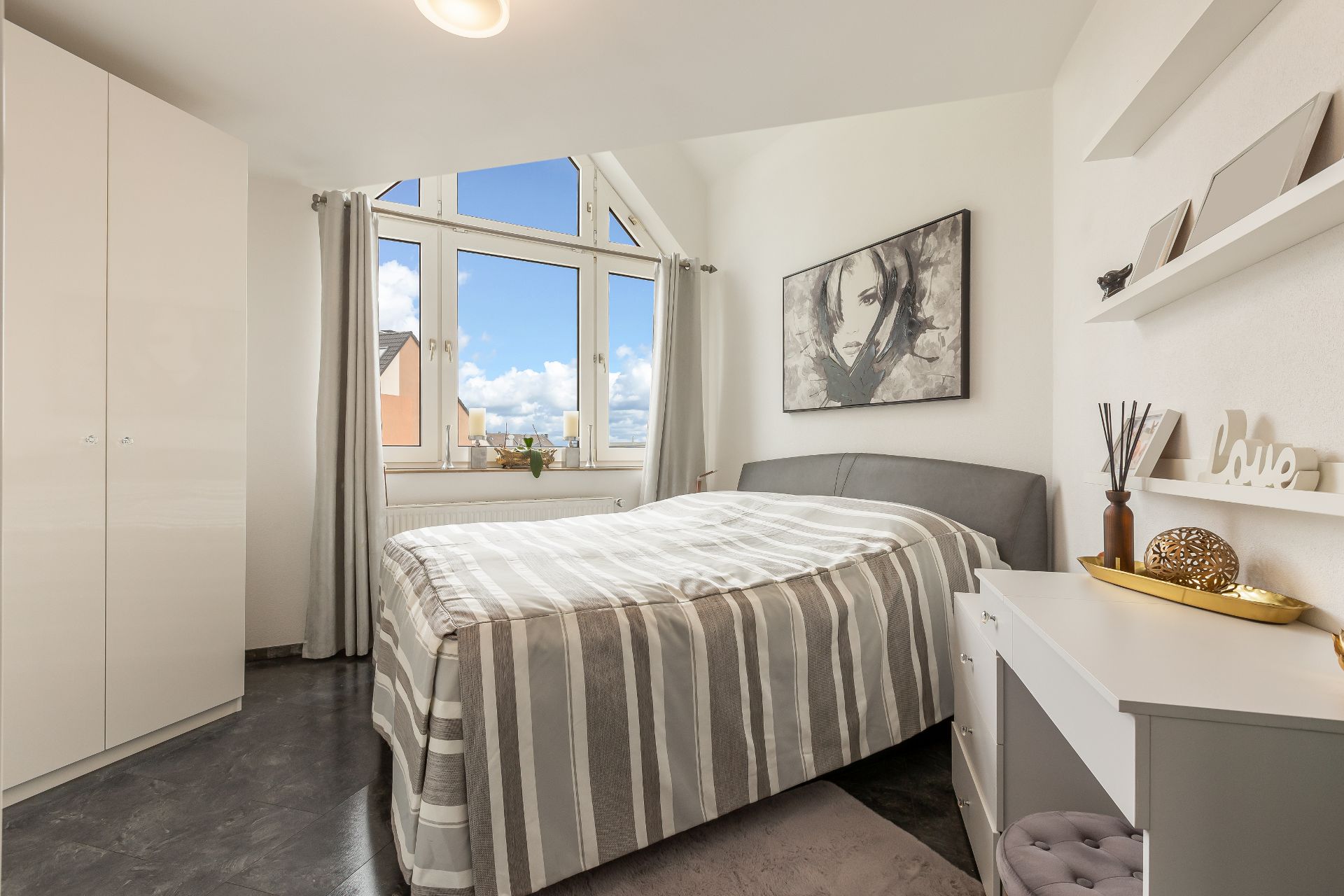 Helles Schlafzimmer mit großem Fenster, Doppelbett, Kleiderschrank und dekorierten Regalen.