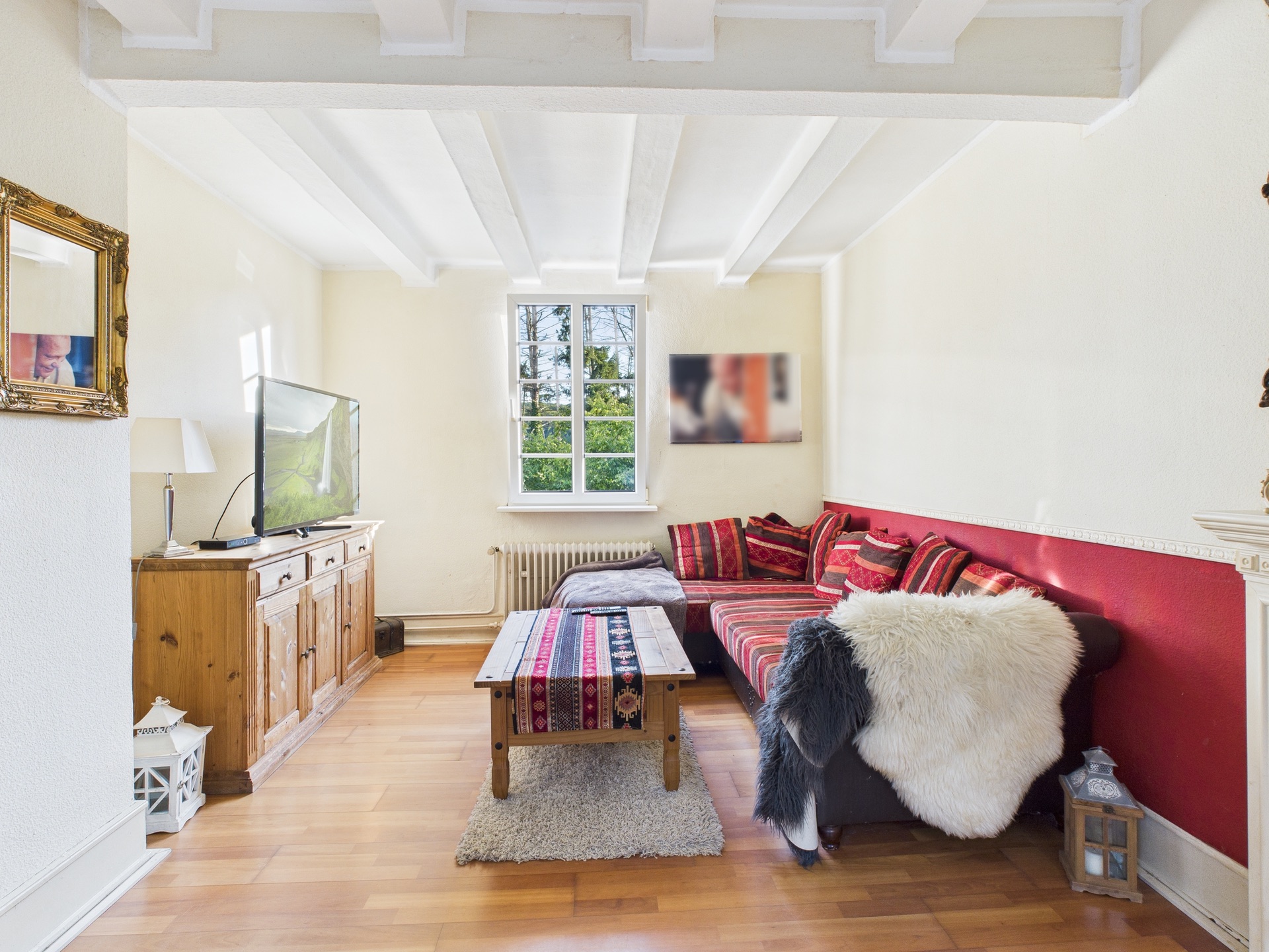 Helles Wohnzimmer mit Ecksofa, Holzmöbeln, Fernseher und Fenster zur Straße.