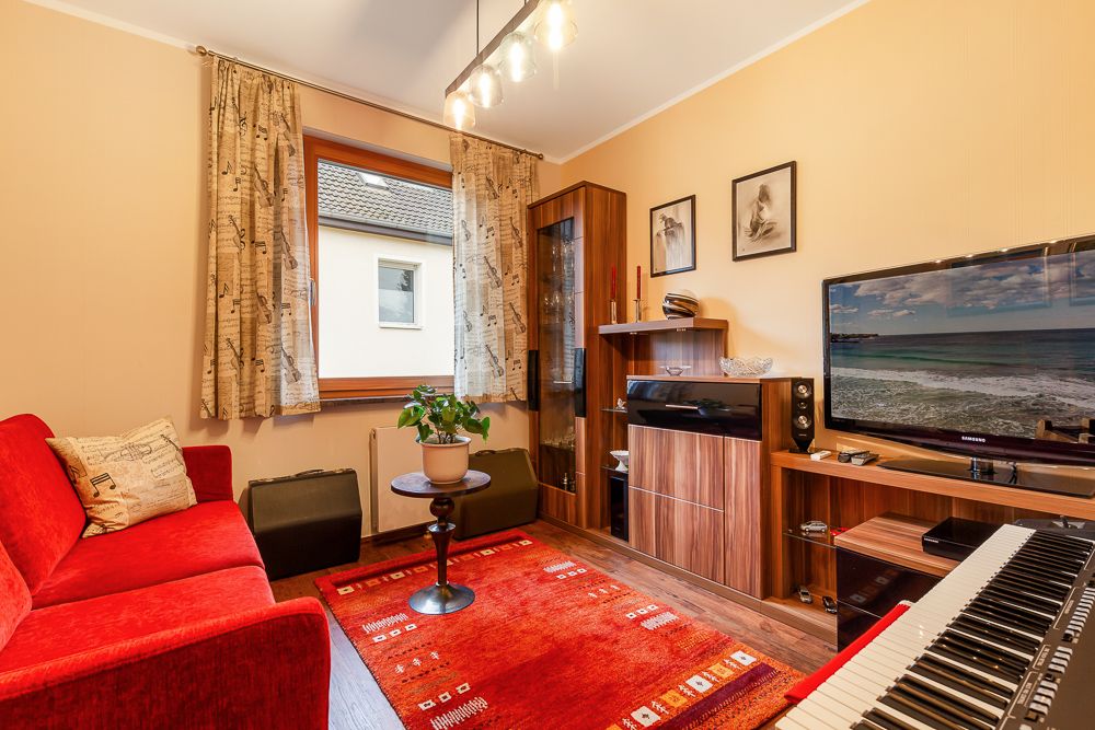 Wohnzimmer mit rotem Sofa, Fernseher, Keyboard, Holzmöbeln und rotem Teppich.