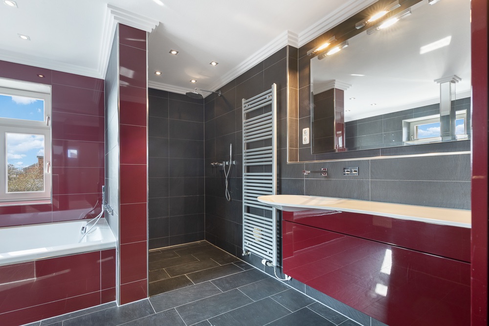 Modernes Badezimmer mit Badewanne, großer Dusche, Spiegel und roten Fliesen.
