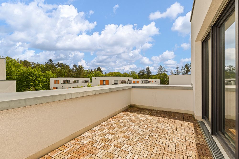 Große, geflieste Terrasse mit Blick auf Bäume und moderne Wohngebäude.