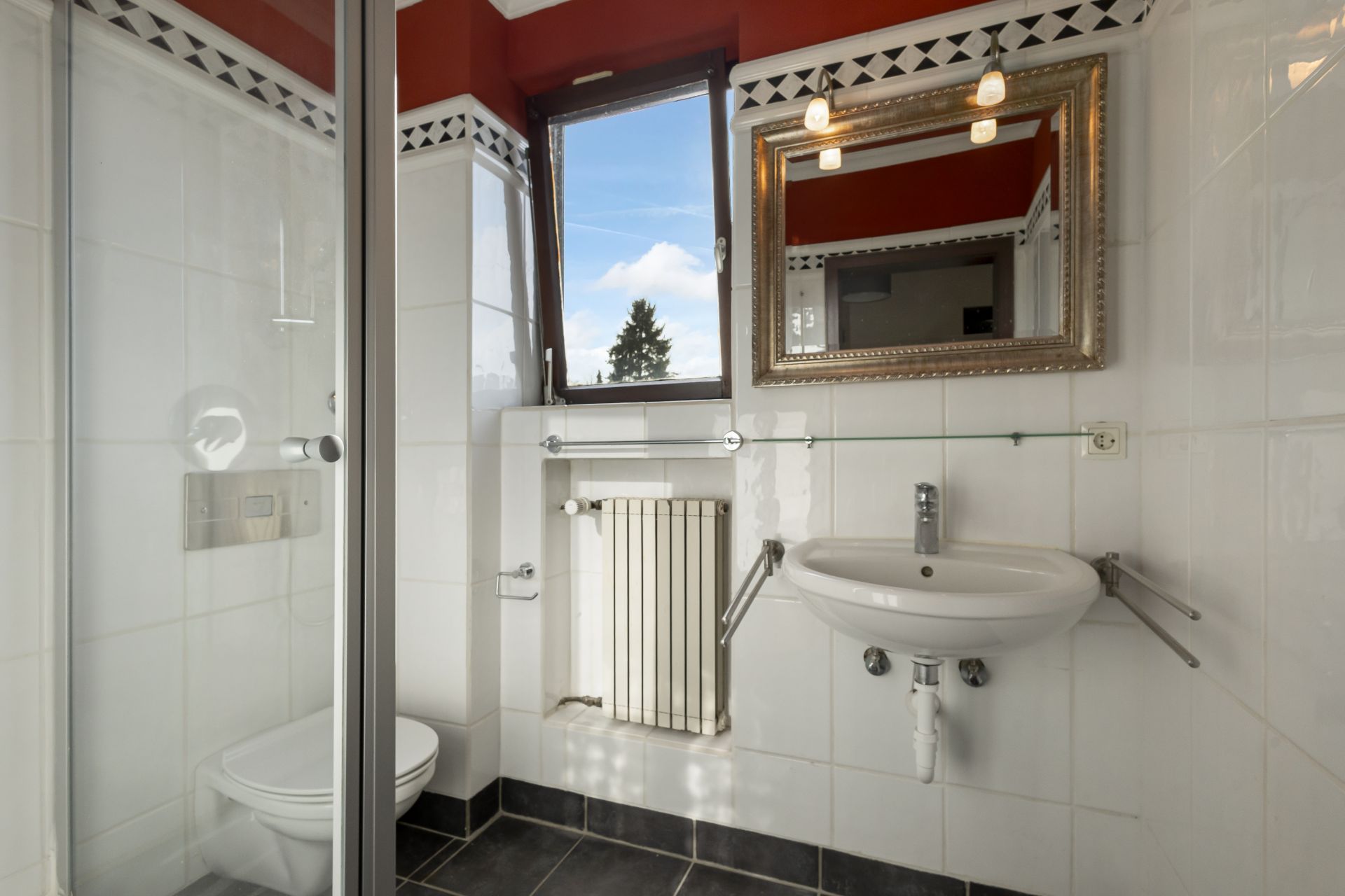 Kleines Badezimmer mit Fenster, Spiegel, Waschbecken, Toilette und Dusche.