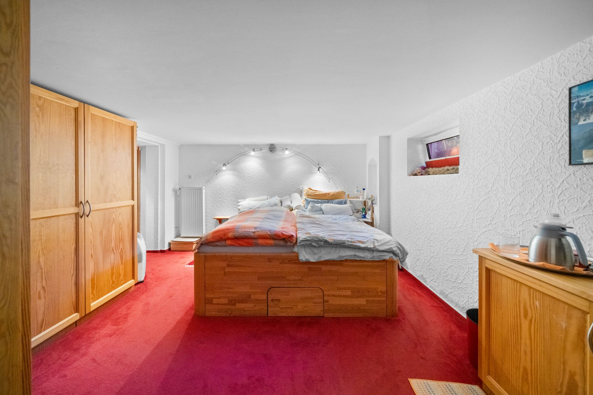 Schlafzimmer mit Doppelbett, rotem Teppich, Holzmöbeln und weißen Wänden.