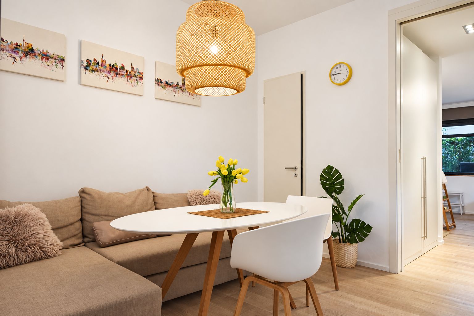 Gemütliches Wohnzimmer mit Sofa, Esstisch, Stühlen, Blumen, Uhr und Bildern an der Wand.