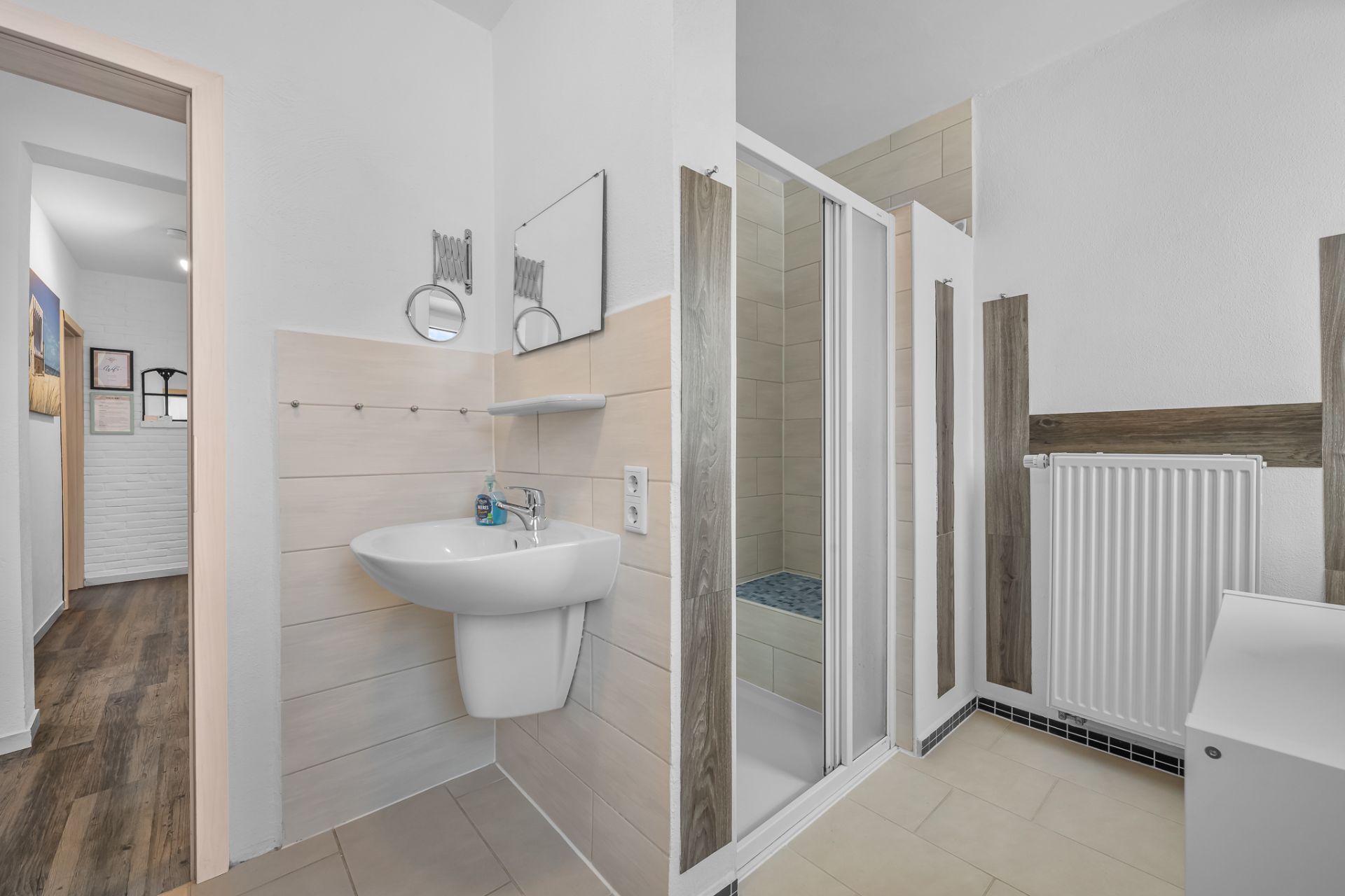 Modernes Badezimmer mit Waschbecken, Spiegel, Dusche und Heizkörper.