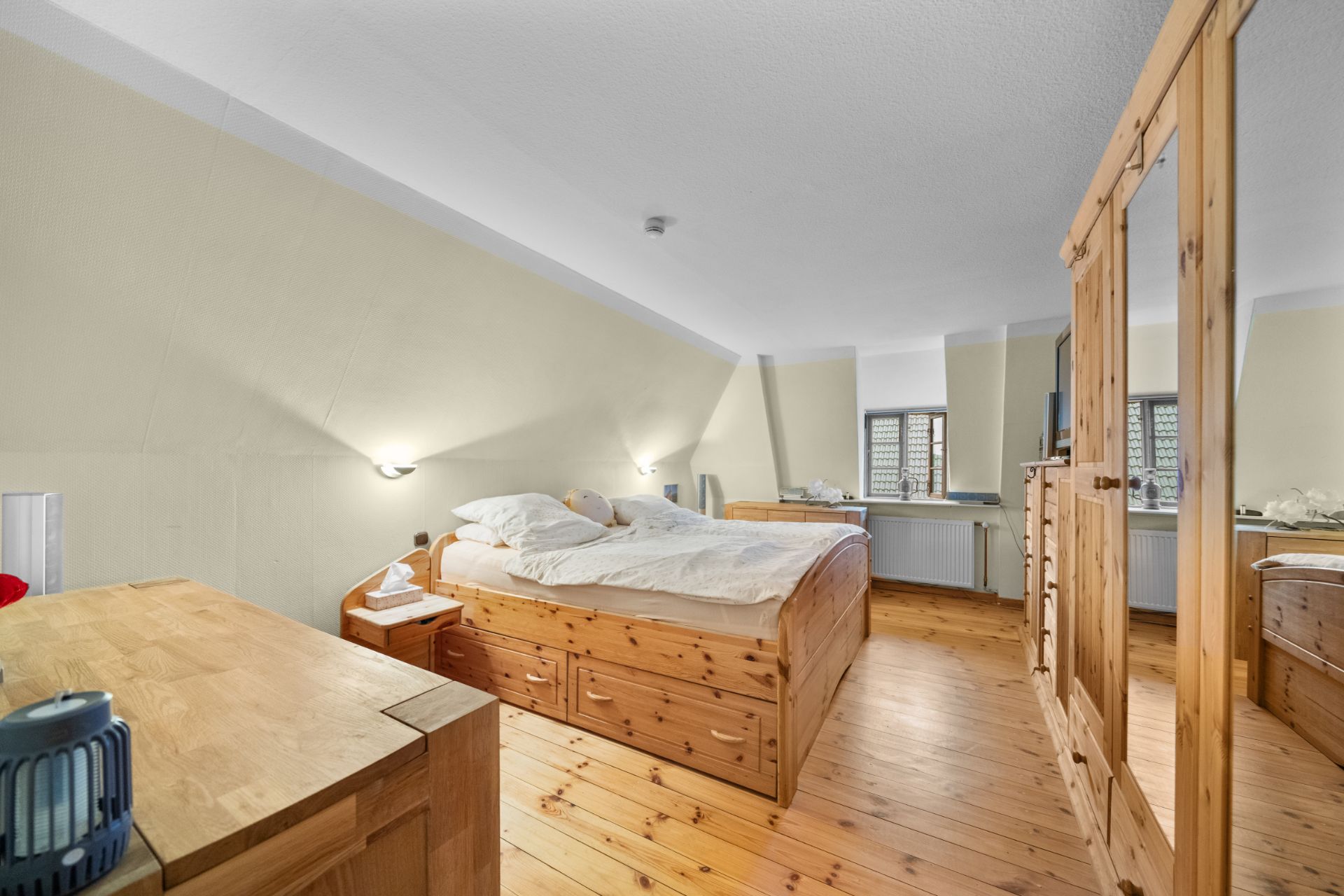 Schlafzimmer mit Holzboden, Doppelbett, Kleiderschrank und Kommode.