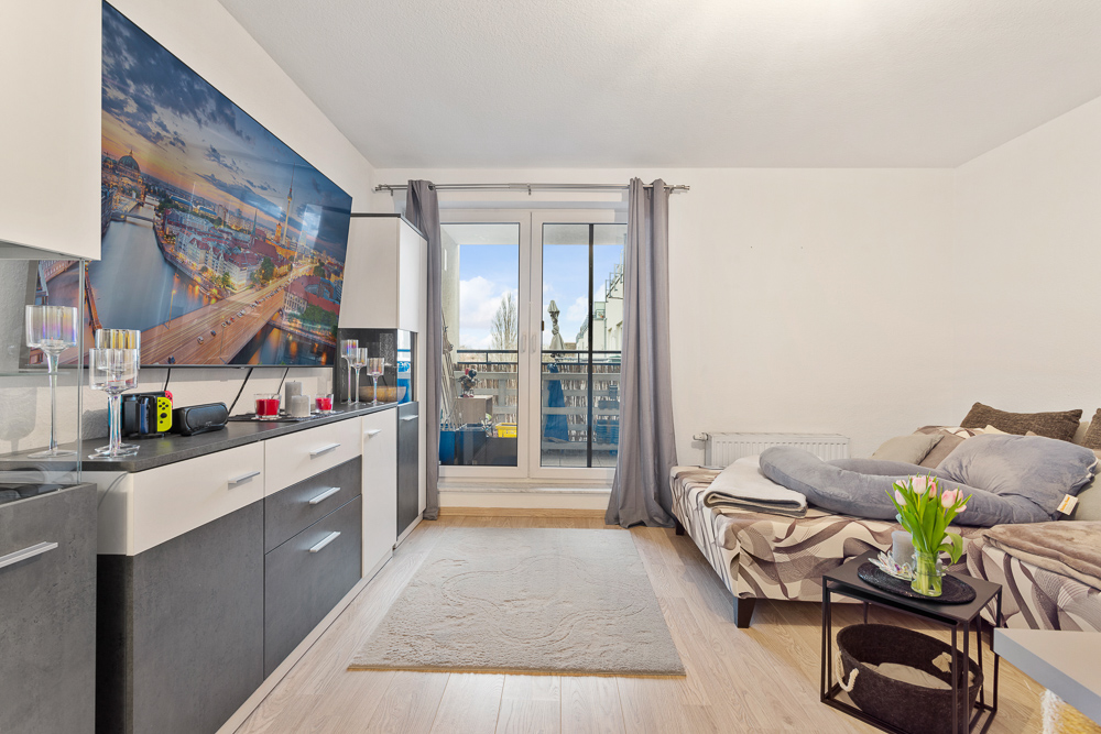 Wohnzimmer mit Schlafsofa, Teppich, Sideboard, großem Bild und Zugang zum Balkon.