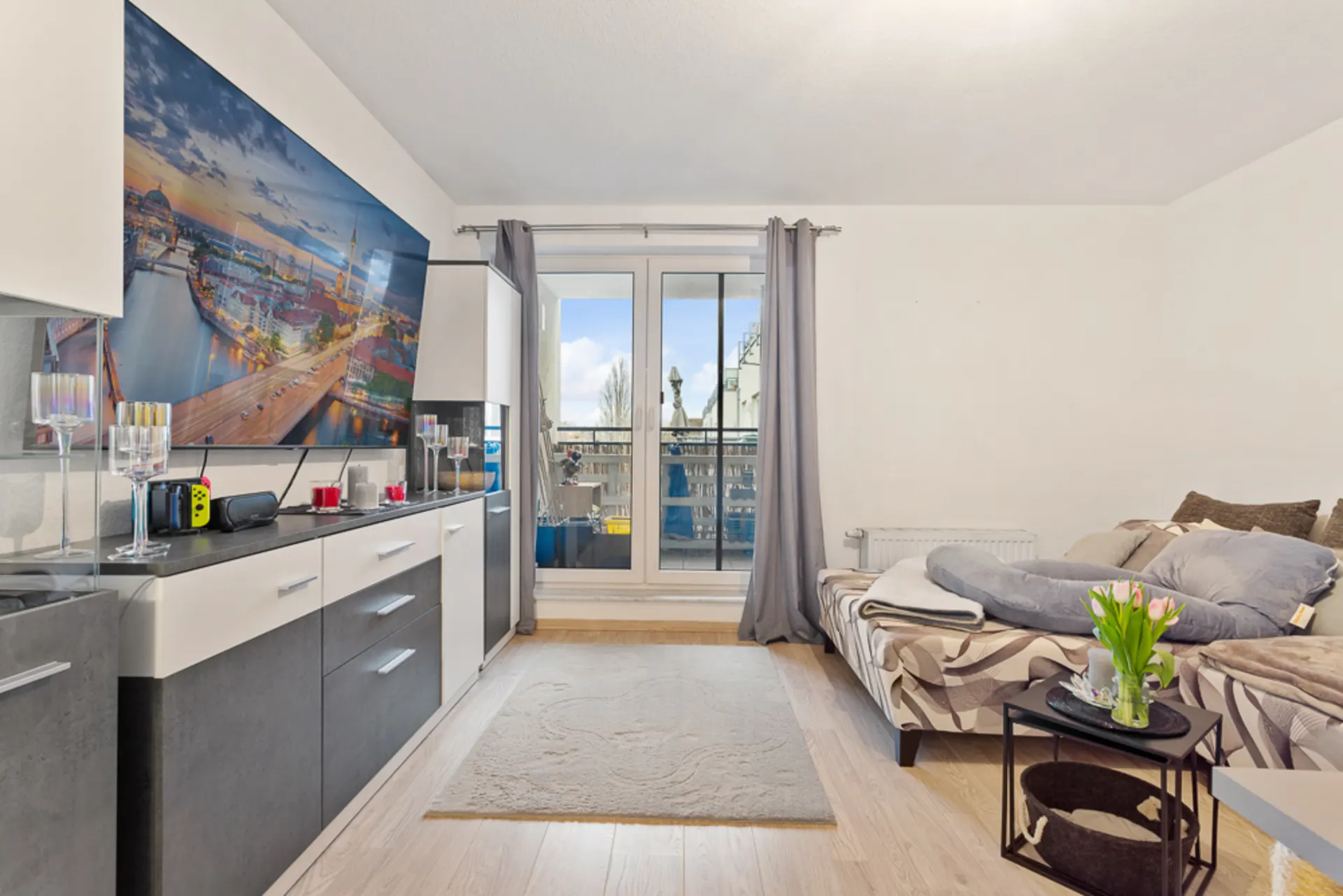 Wohnzimmer mit Schlafsofa, Teppich, Sideboard, großem Bild und Zugang zum Balkon.