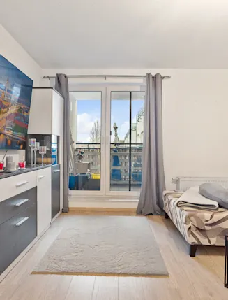 Wohnzimmer mit Schlafsofa, Teppich, Sideboard, großem Bild und Zugang zum Balkon.