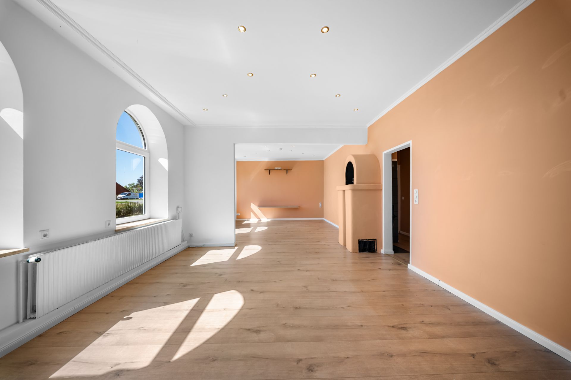 Heller Wohnraum mit Holzboden, großen Fenstern und orangefarbener Wand.