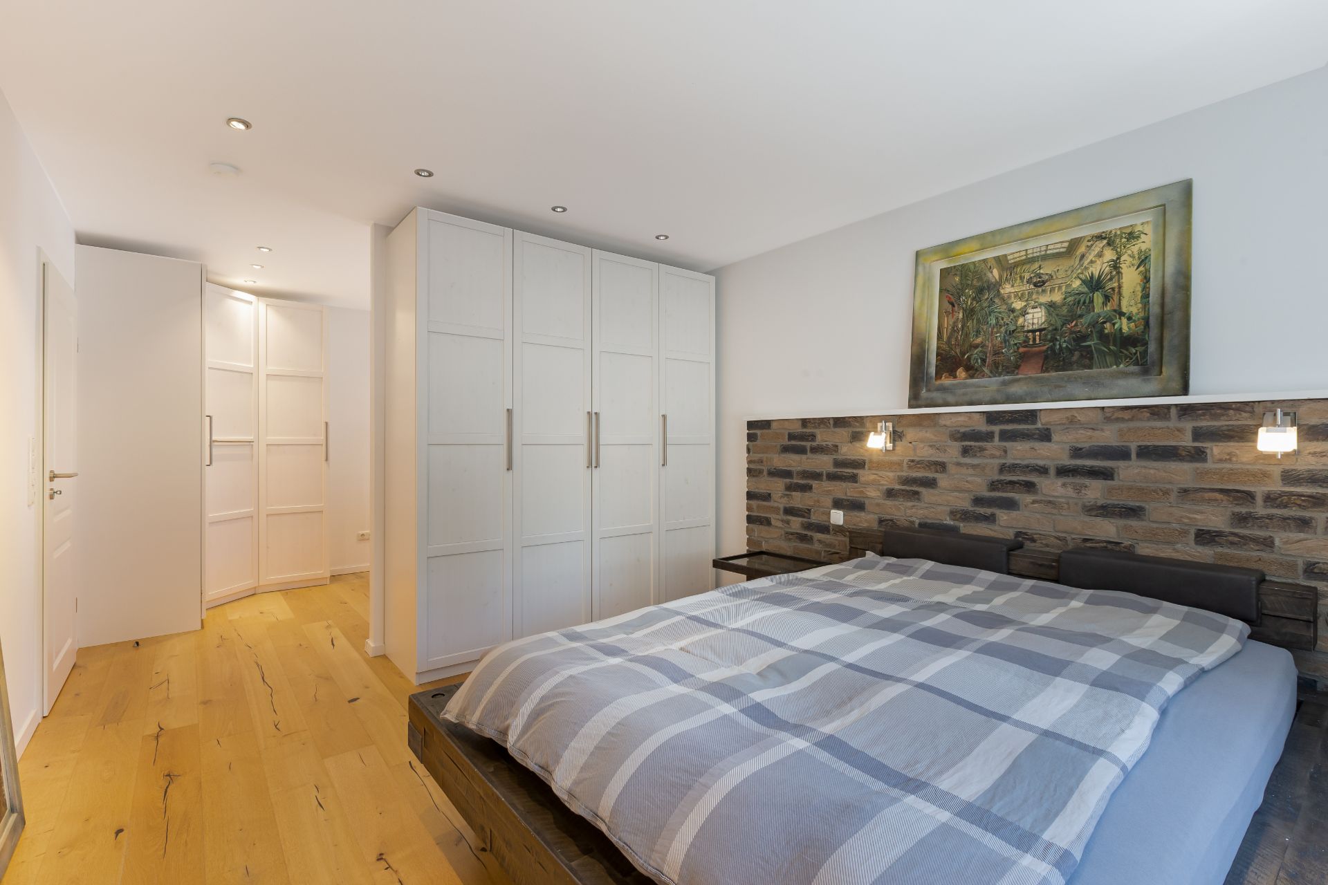 Helles Schlafzimmer mit Doppelbett, Einbauschränken und gemauerter Wand hinter dem Bett.