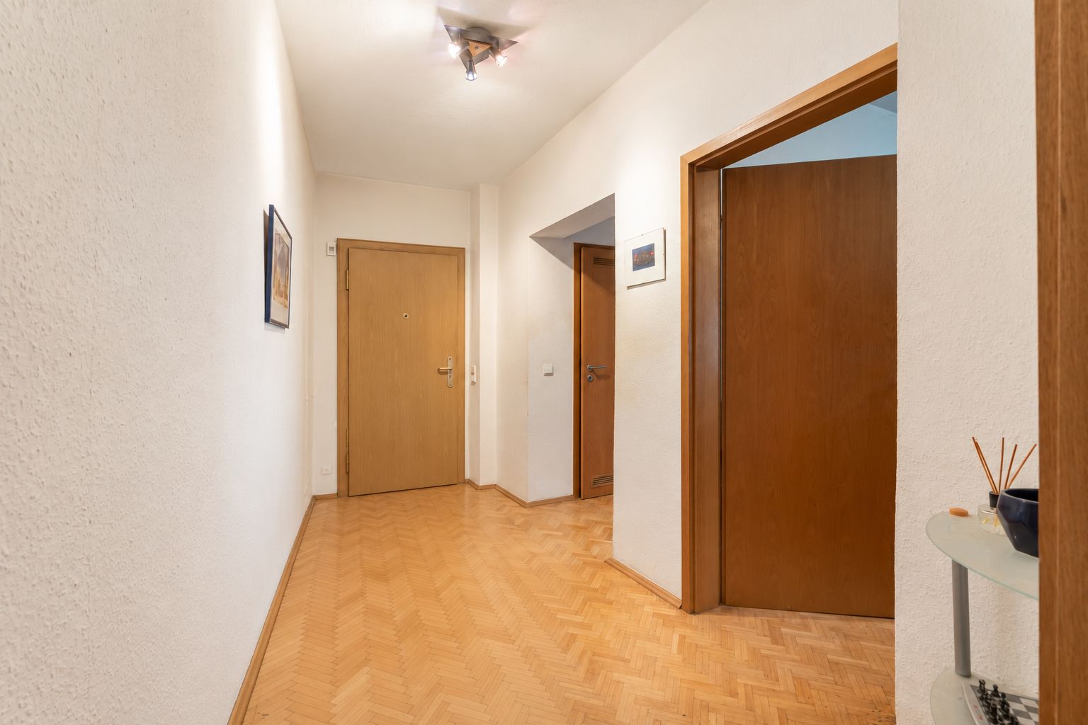 Heller Flur mit Holztüren, Parkettboden und Bildern an den Wänden.