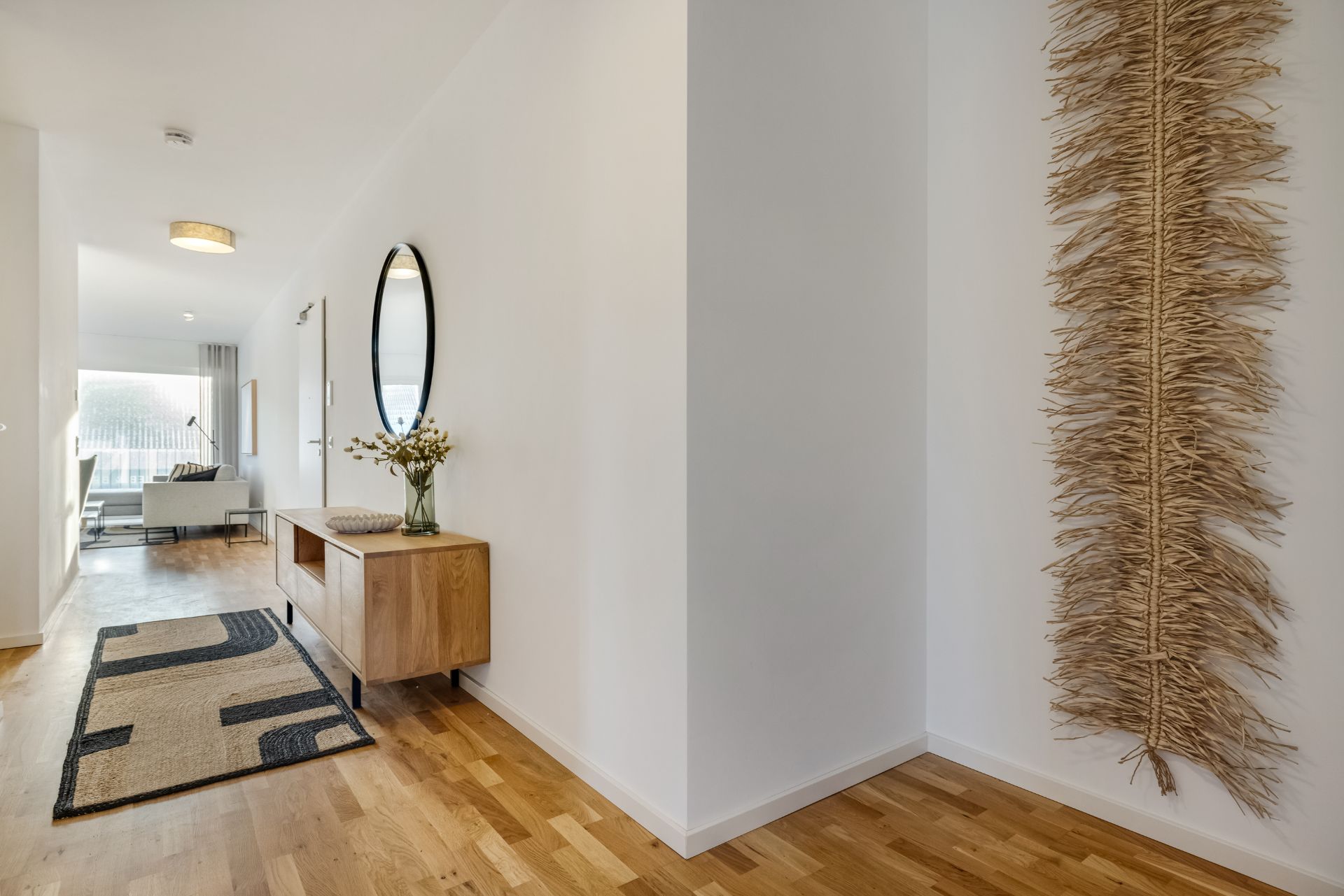Heller Flur mit Holzfußboden, Wanddeko, Teppich und Kommode mit Spiegel und Vase.