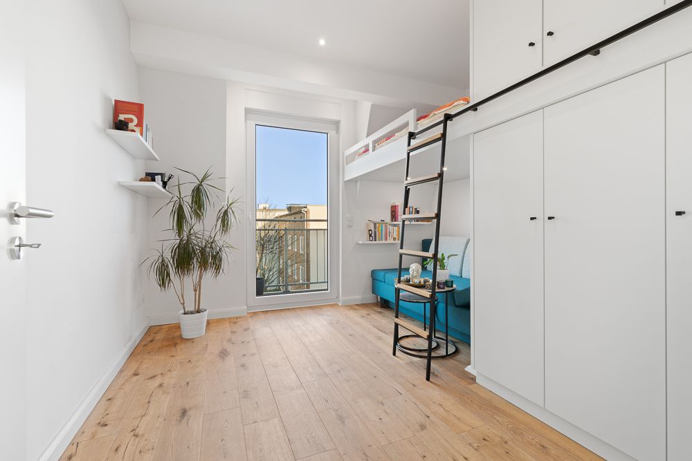 Modernes Zimmer mit Hochbett, Holzboden, Kleiderschrank, Grünpflanze und großem Fenster.