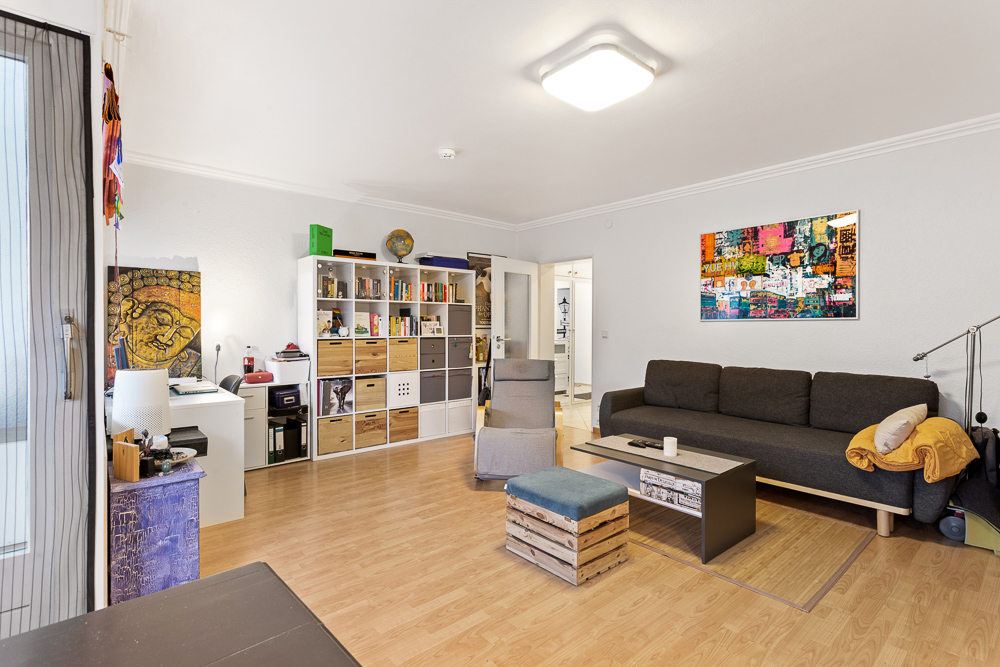 Wohnzimmer mit schwarzem Sofa, Regal, Schreibtisch und farbenfrohem Wandbild.